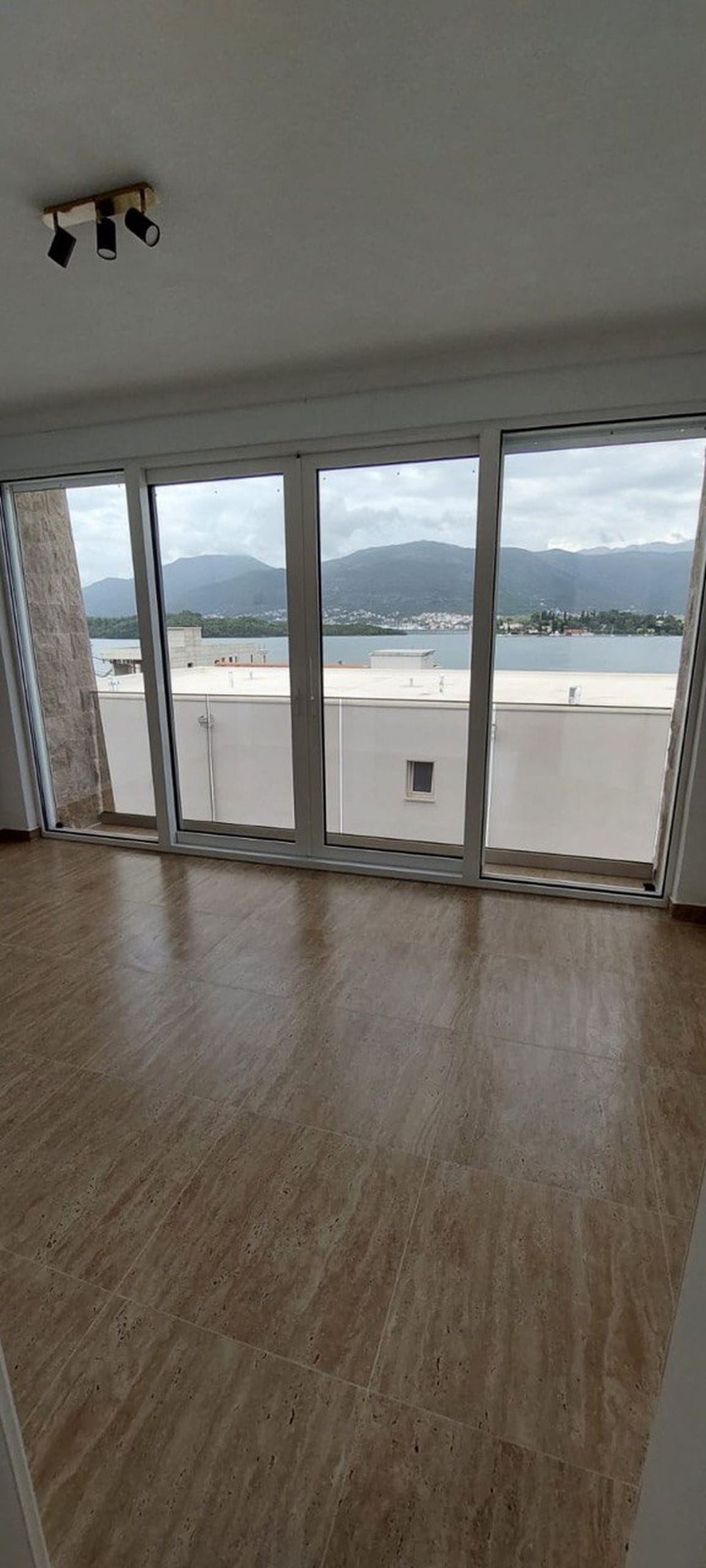 Dnevna soba s panoramskim prozorima i pogledom na more i planine u taunhausu, Luštica, Crna Gora. Svetao enterijer s pločicama.
