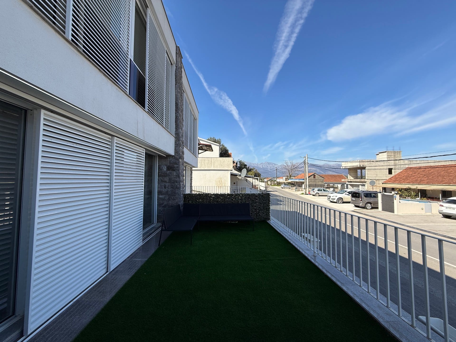 Terasa kuće u nizu u Đuraševićima, Crna Gora: balkon sa veštačkom travom, nameštajem i pogledom na planine i ulicu.