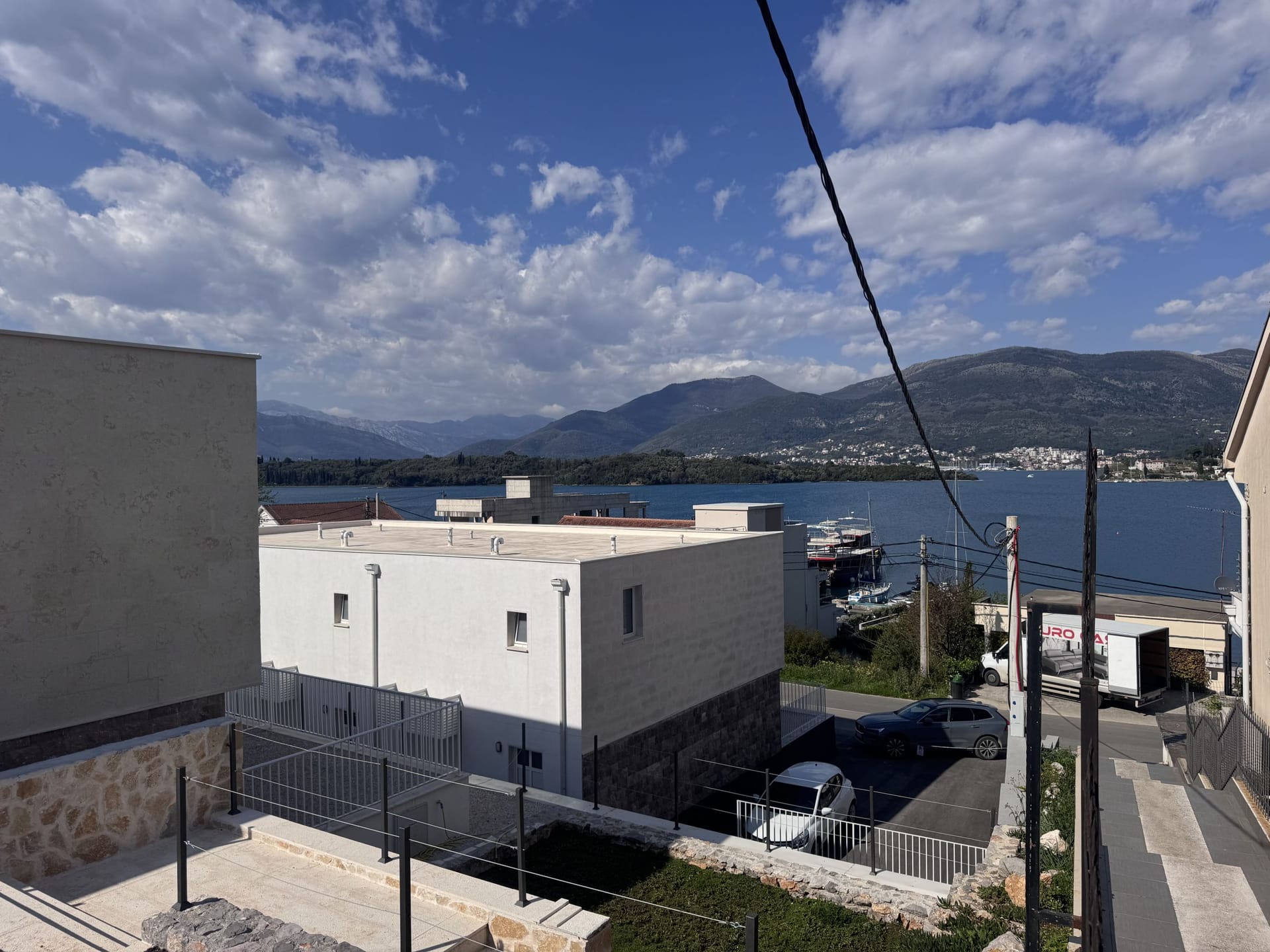 Pogled na more i planine sa terase kuće u nizu na Luštici, Crna Gora: savremena arhitektura, parking i morski pejzaž.