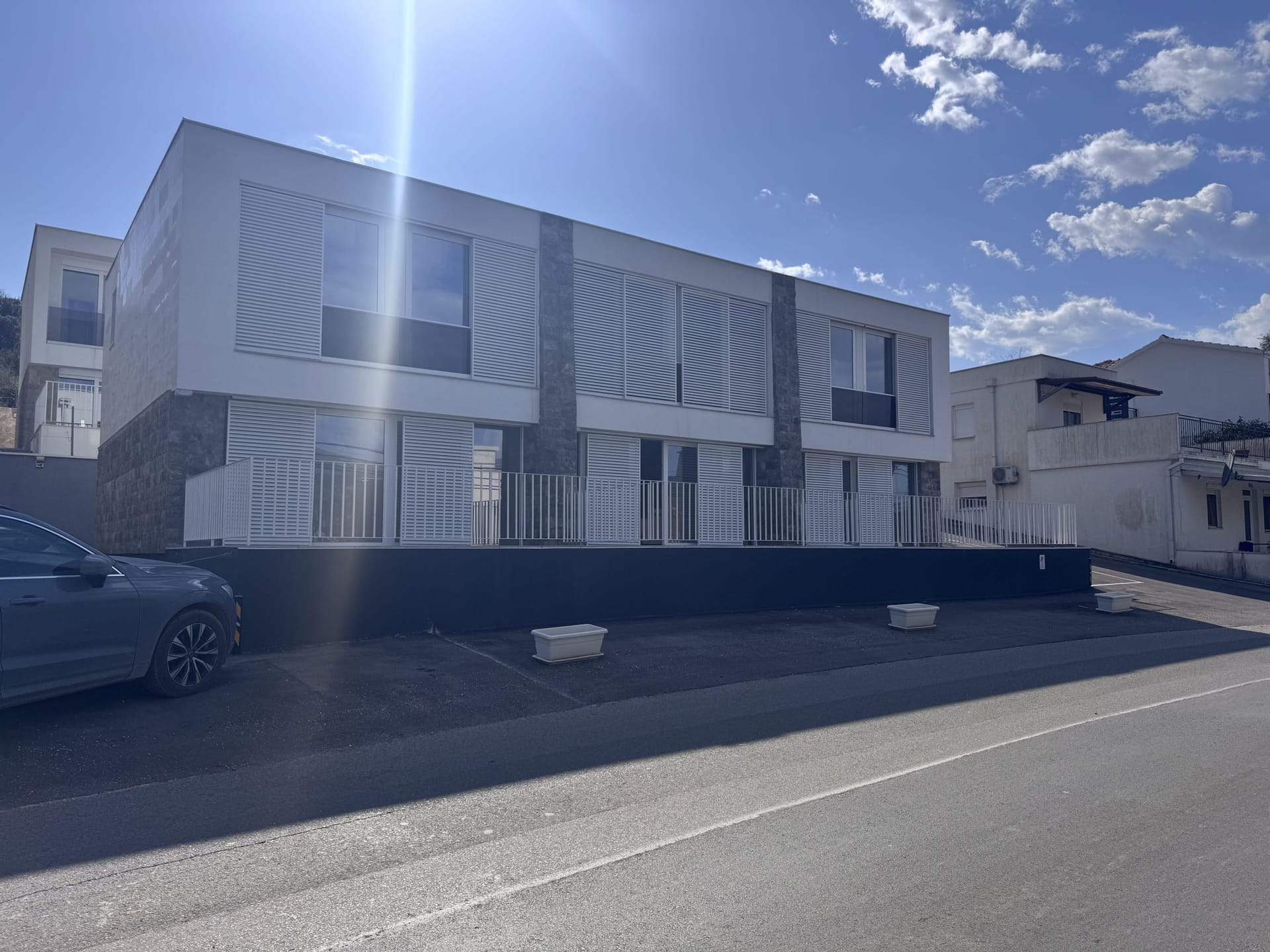 Moderan dvospratni townhouse sa belom fasadom i žaluzinama u Luštici, Crna Gora, pogled sa ulice na parking.