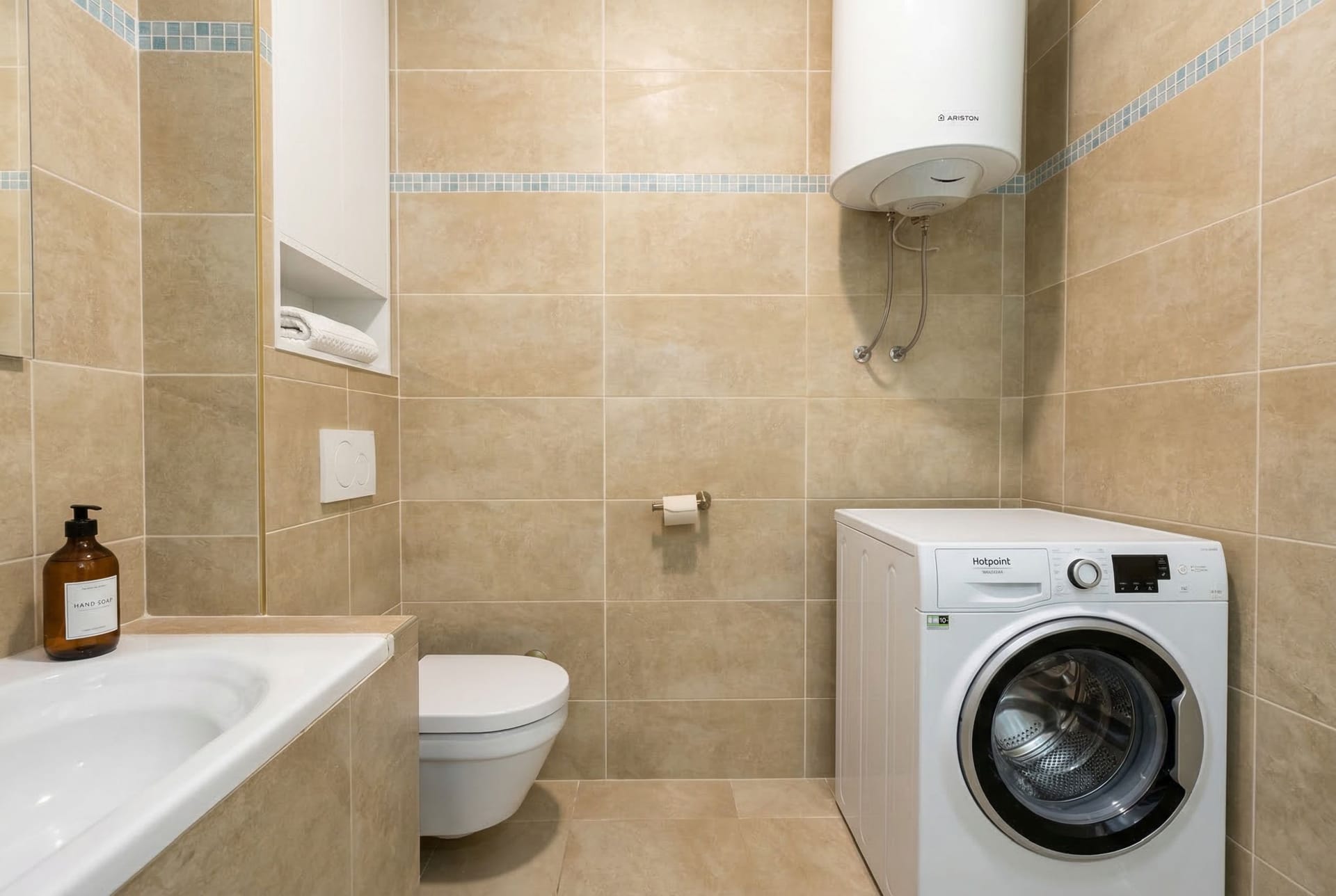 Kupatilo u stanu u Budvi, Crna Gora: bež pločice, veš mašina Hotpoint, bojler Ariston i sanitarije.