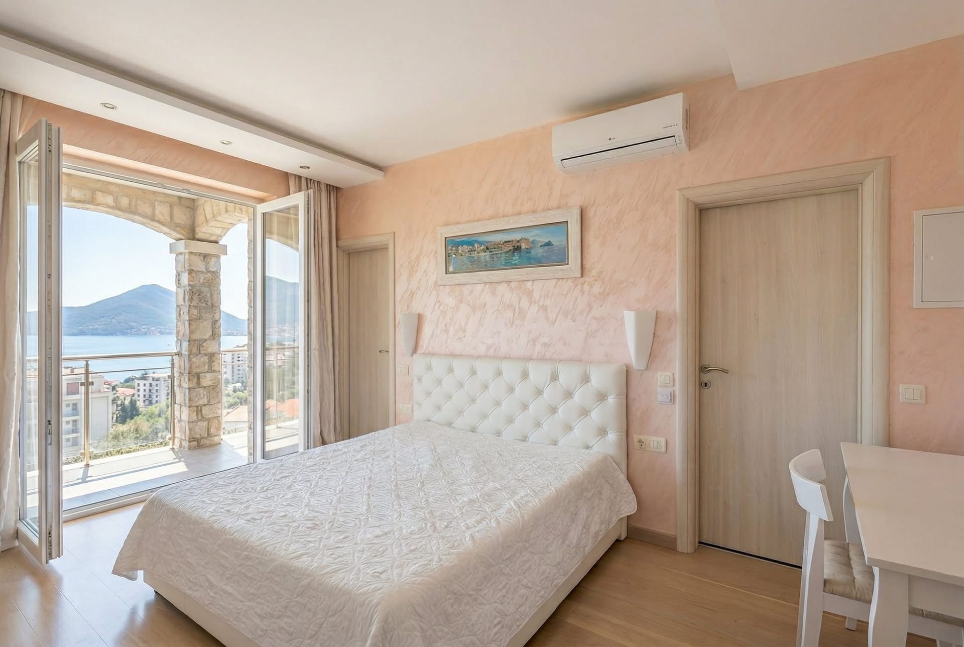 Spavaća soba u stanu u Bečićima, Crna Gora: beli krevet, terasa s panoramskim pogledom na more i planine, svetao enterijer.