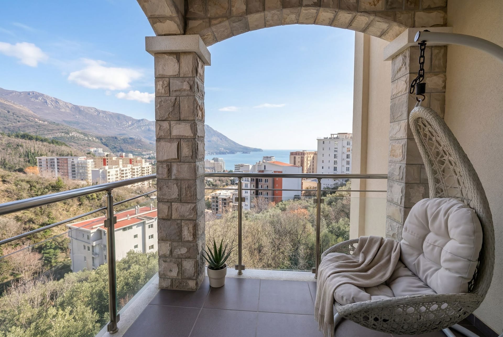 Balkon sa visećom foteljom i pogledom na more i planine u stanu u Bečićima, Crna Gora. Kamena obloga stubova.