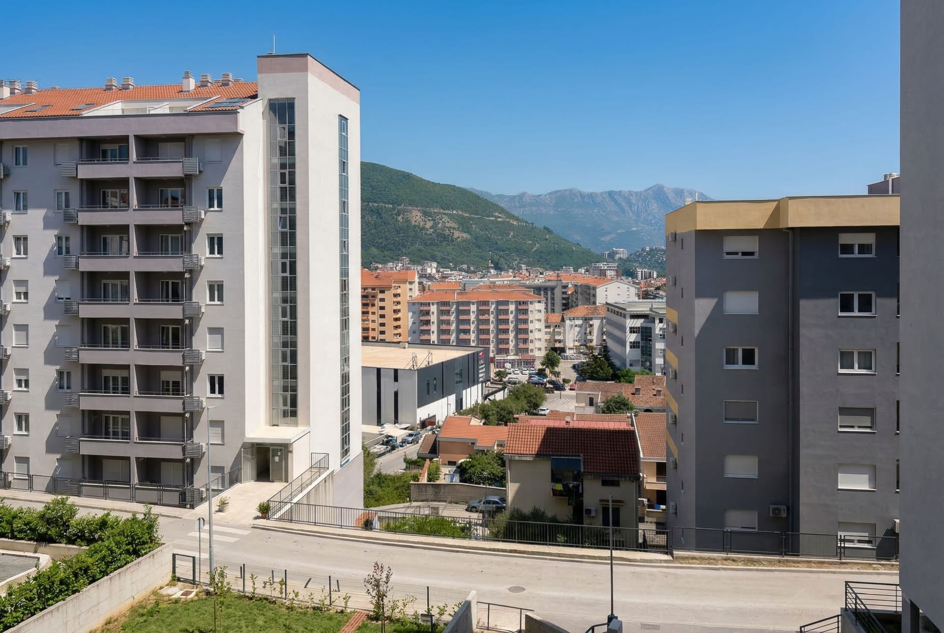 Pogled na moderne stambene zgrade i planinski pejzaž kroz prozor stana u Budvi, Crna Gora.