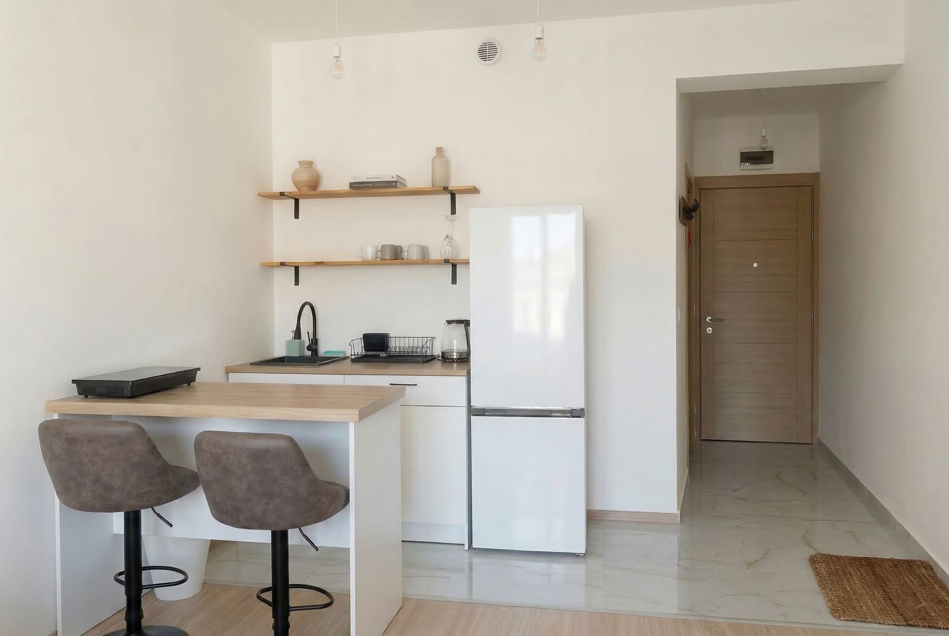 Kuhinja-studio sa barskim pultom i belim nameštajem u stanu u Budvi, Crna Gora. Moderan enterijer sa pločicama na podu.