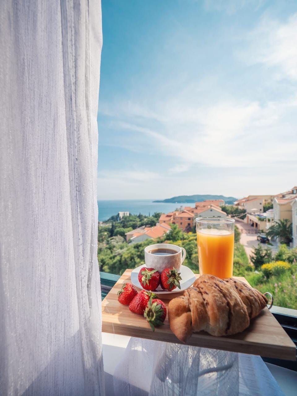 Doručak na balkonu stana u Bečićima, Crna Gora, sa panoramskim pogledom na more, planine i mediteranski pejzaž.