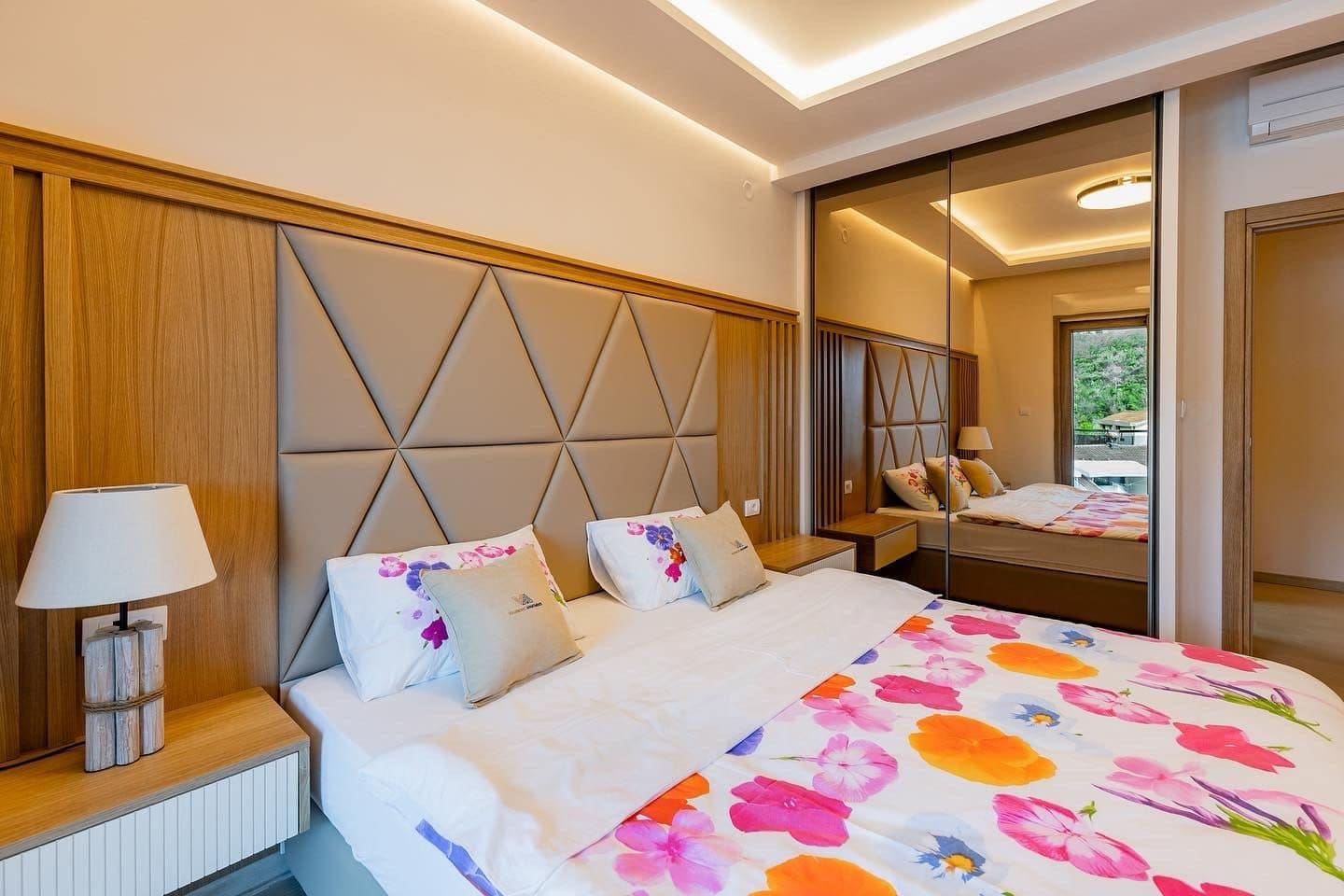 Modern bedroom in a penthouse in Pržno, Montenegro: double bed, upholstered headboard, and mirrored sliding wardrobe.