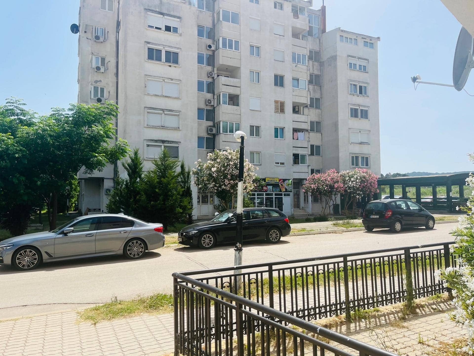 Многоэтажный жилой дом в Сутоморе, Черногория: вид на фасад здания, придомовую территорию и парковку у входа.