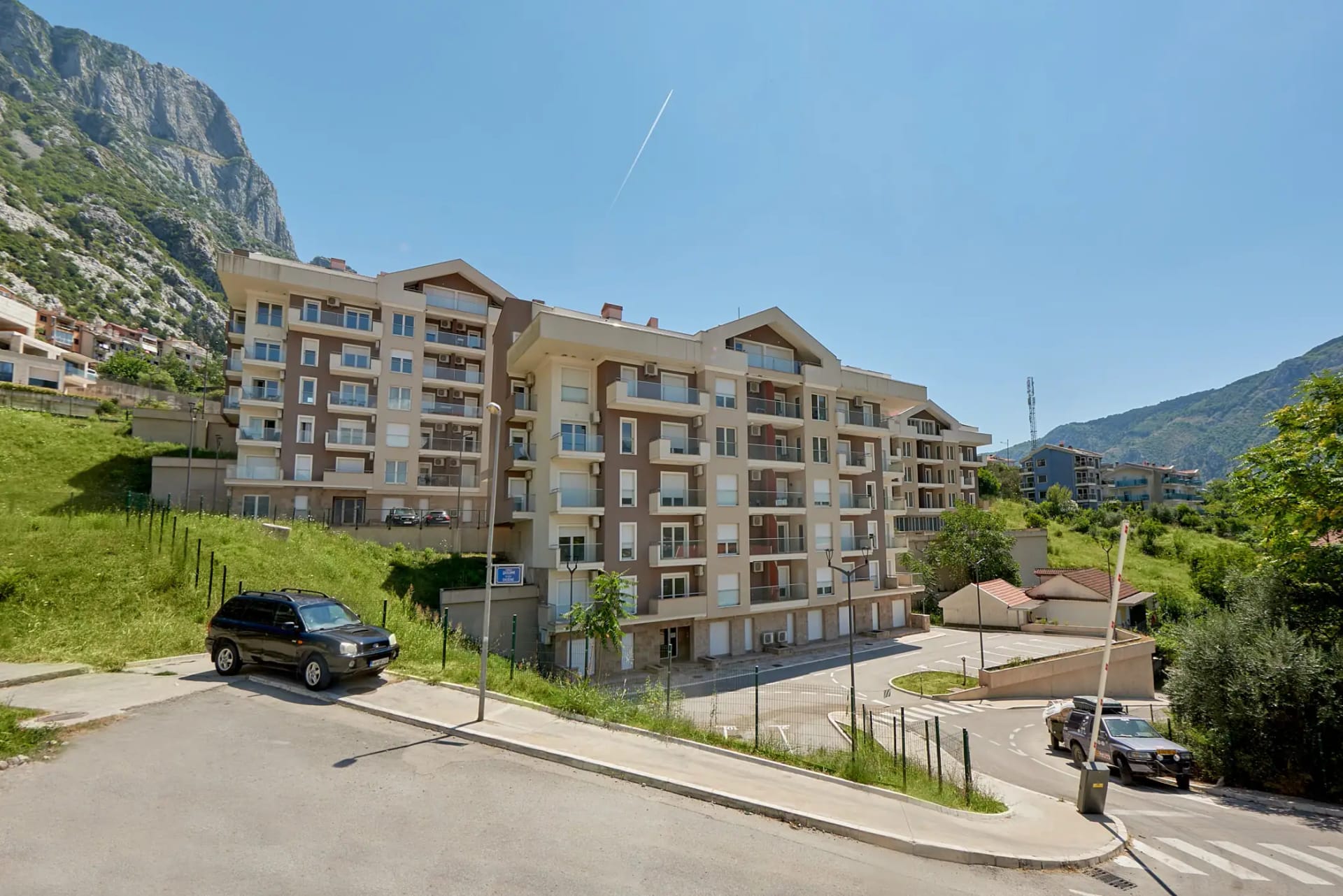 Modern residential complex in Dobrota, Montenegro: view of the building with balconies, parking, and mountain scenery.