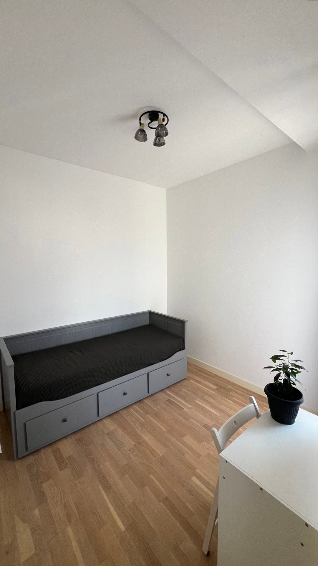 Bedroom in an apartment in Dobrota, Montenegro: gray bed with drawers, light parquet flooring, white walls, and a desk.