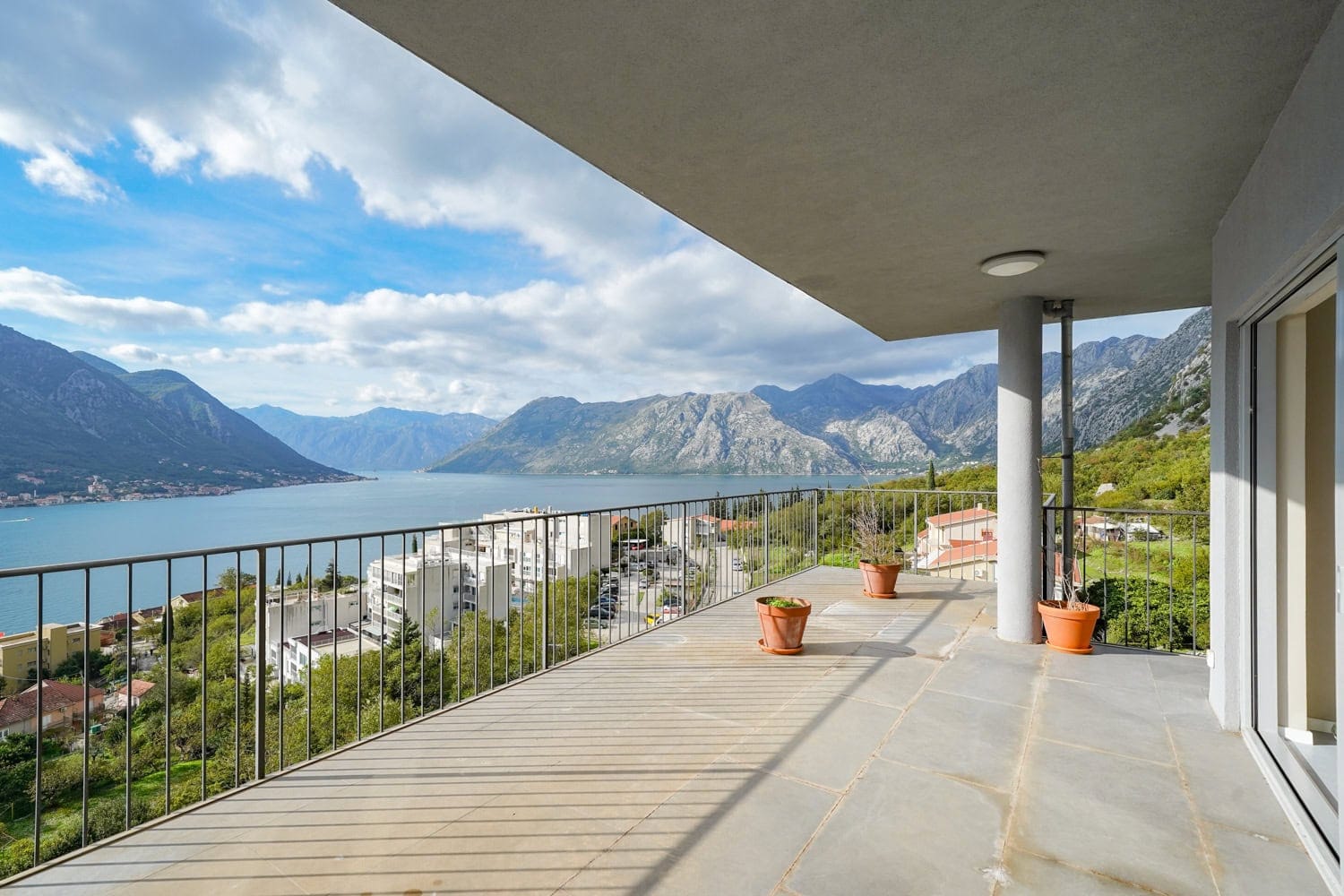 Spacious balcony with panoramic views of Kotor Bay and the mountains, apartment in Dobrota, Montenegro, stone floor.