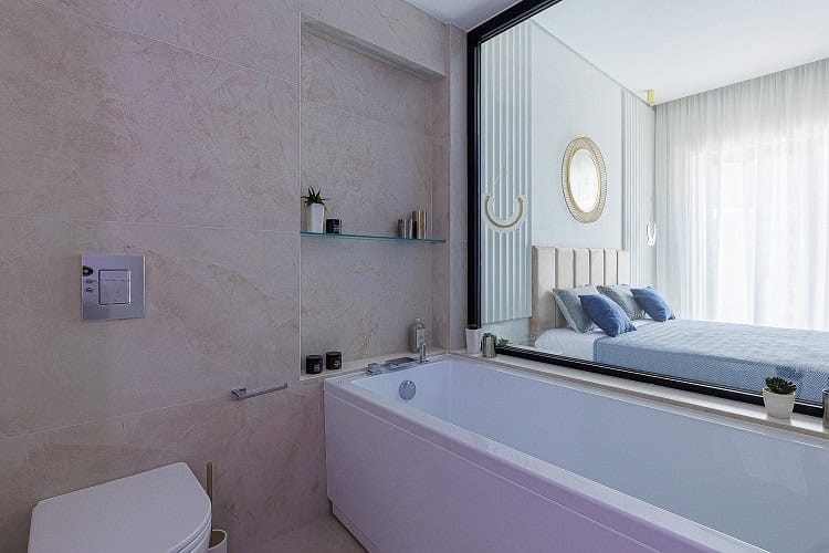 Salle de bains moderne avec fenêtre panoramique sur la chambre, appartement à Bečići, Monténégro. Carrelage clair et décoration élégante.