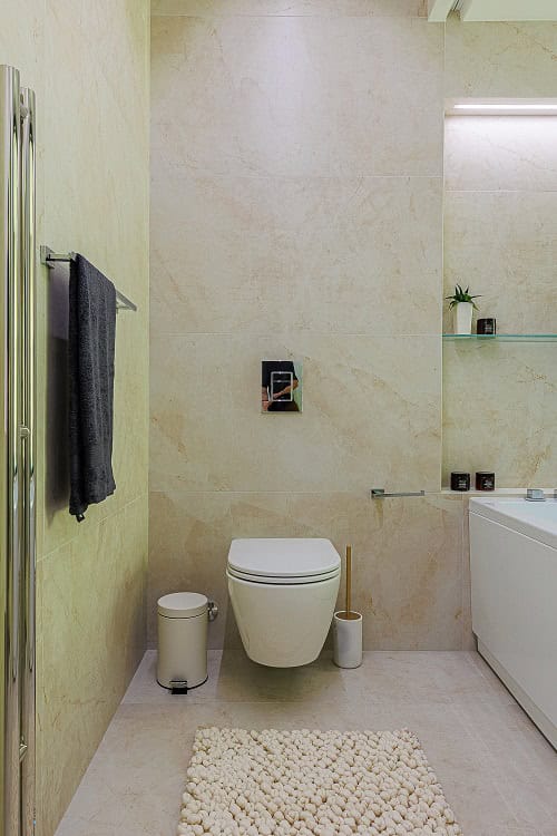 Salle de bains moderne dans un appartement à Bečići, Monténégro : carrelage beige, WC suspendu et sèche-serviettes.