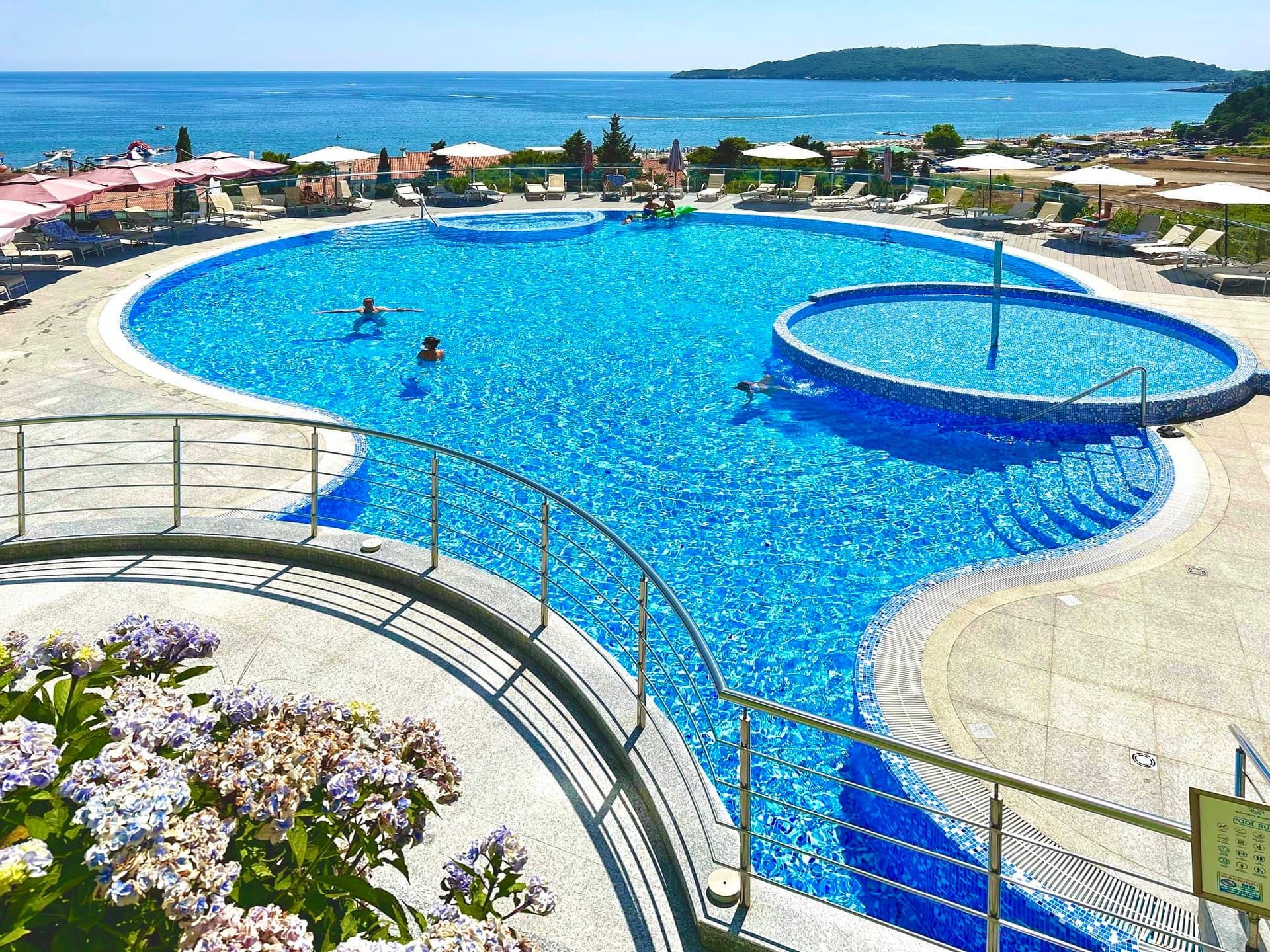 Piscine extérieure avec vue sur la mer dans un complexe résidentiel à Bečići, Monténégro : espace détente avec chaises longues et terrasse.