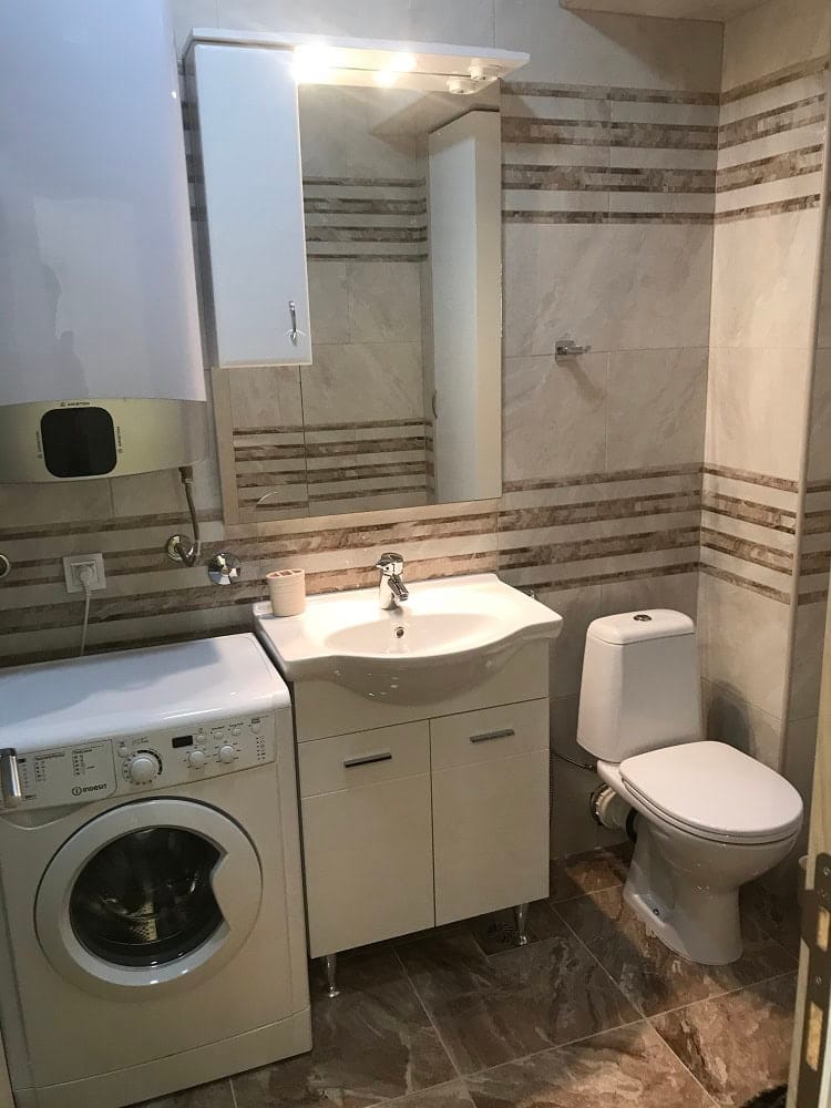 Ванная комната в квартире, Добрые Воды, Черногория: плитка, раковина с тумбой, зеркало и стиральная машина.