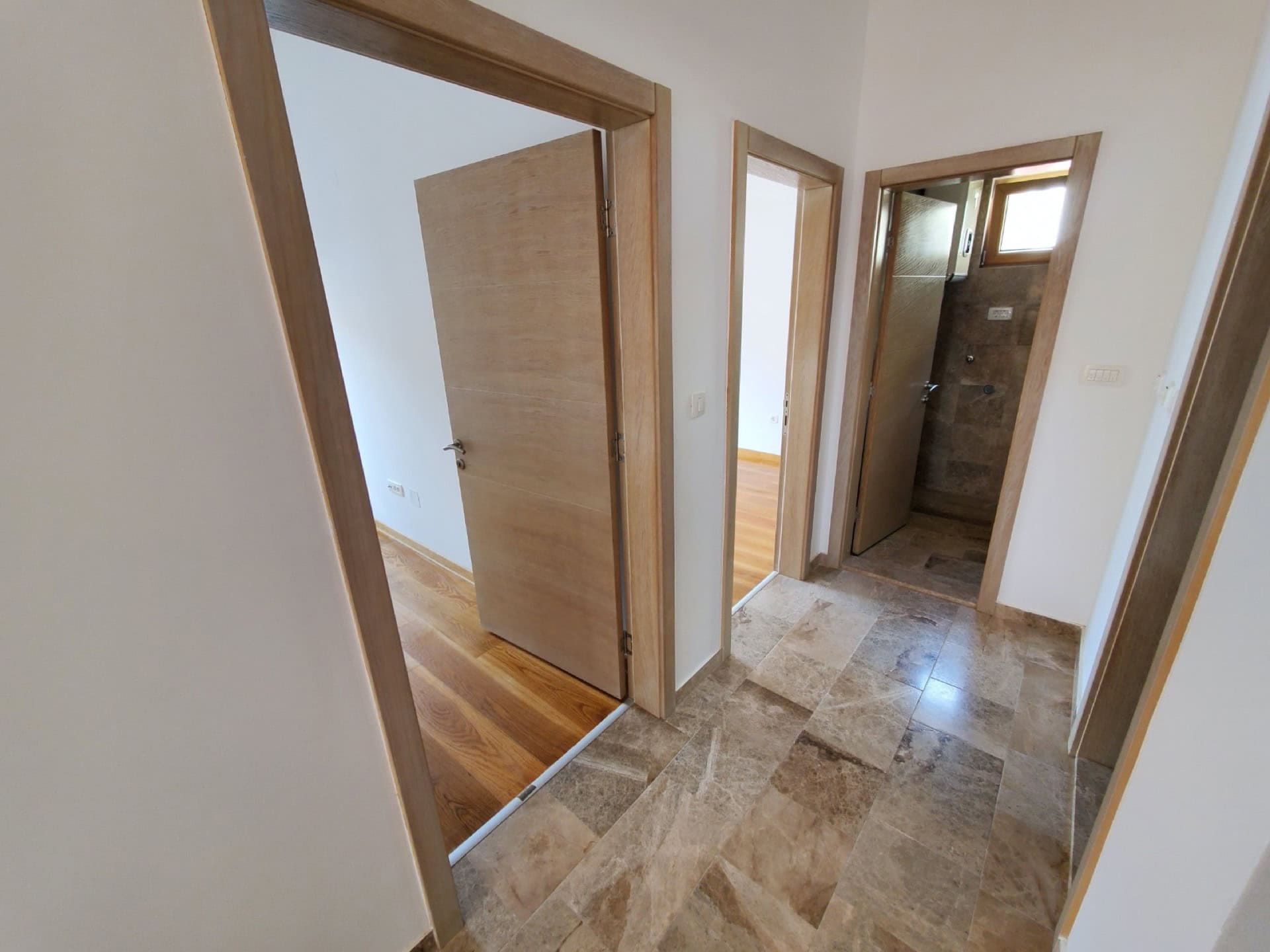 Hallway in a penthouse in Pržno, Montenegro: marble floor, light walls, and interior doors made of natural wood.
