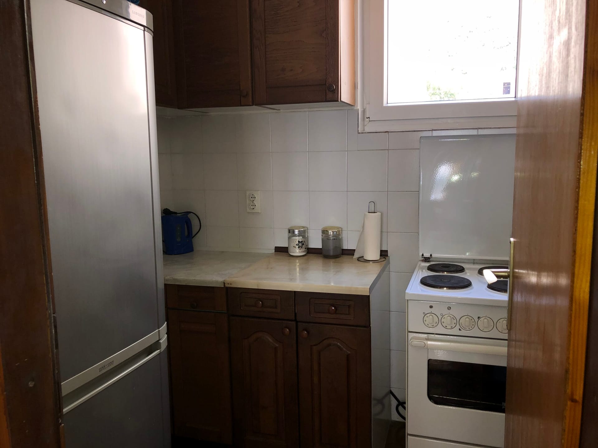 Compact kitchen with wooden cabinets, a stove and a refrigerator in an apartment for sale, Baošići, Montenegro.