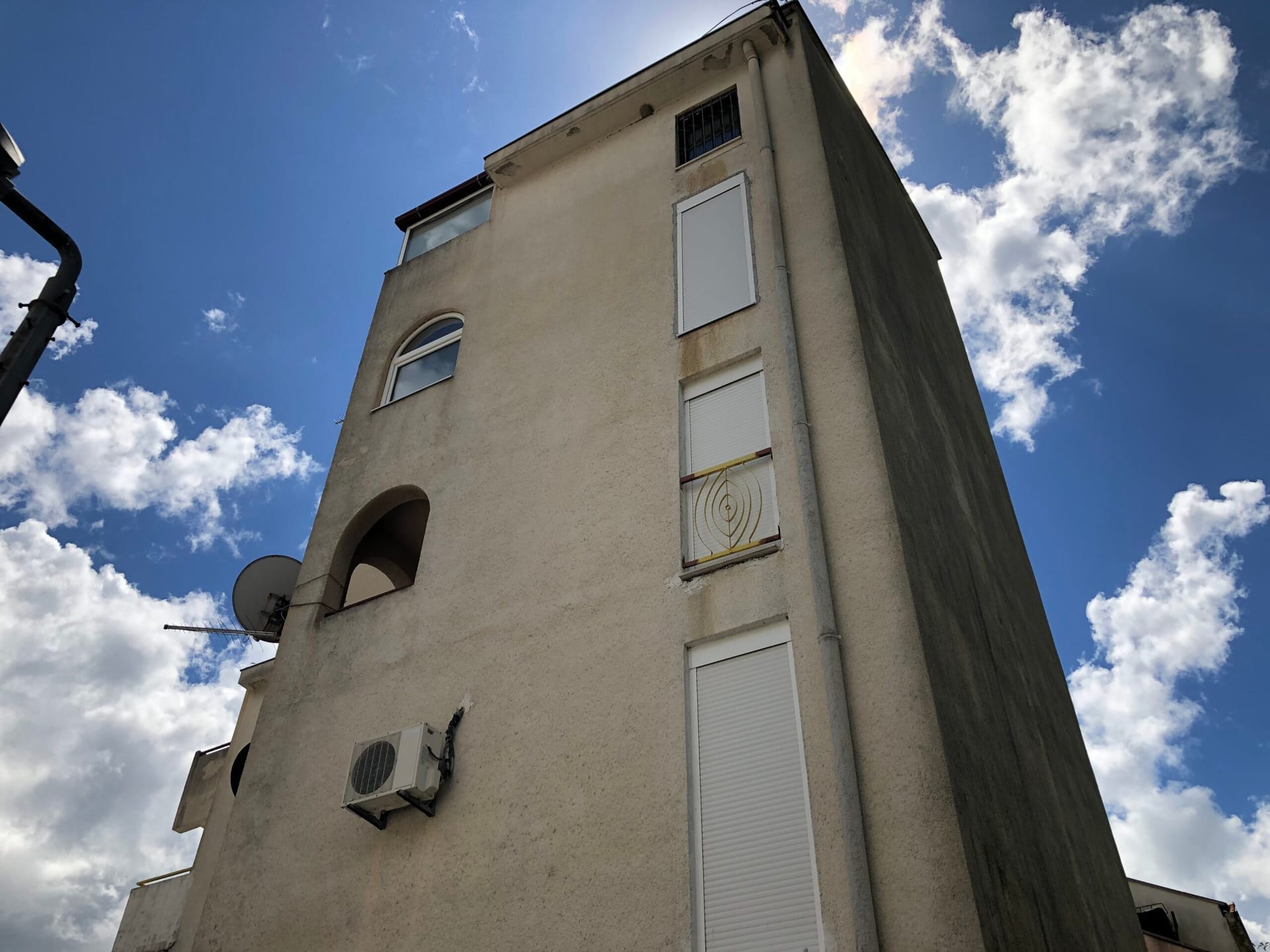Facade of an apartment building in Baošići, Montenegro: view of the building with balconies, windows with shutters, and an air conditioner.
