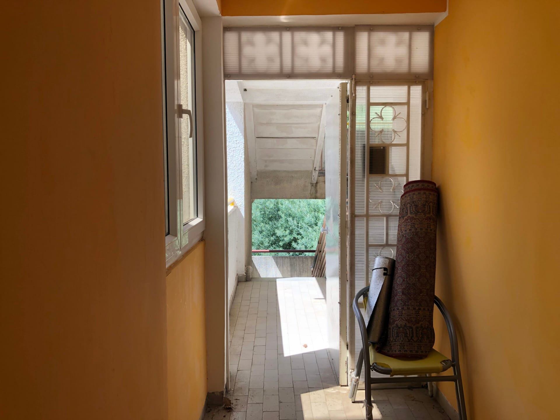 Balcony with yellow walls and a view of greenery in an apartment, Baošići, Montenegro: tiled floor and metal furniture.