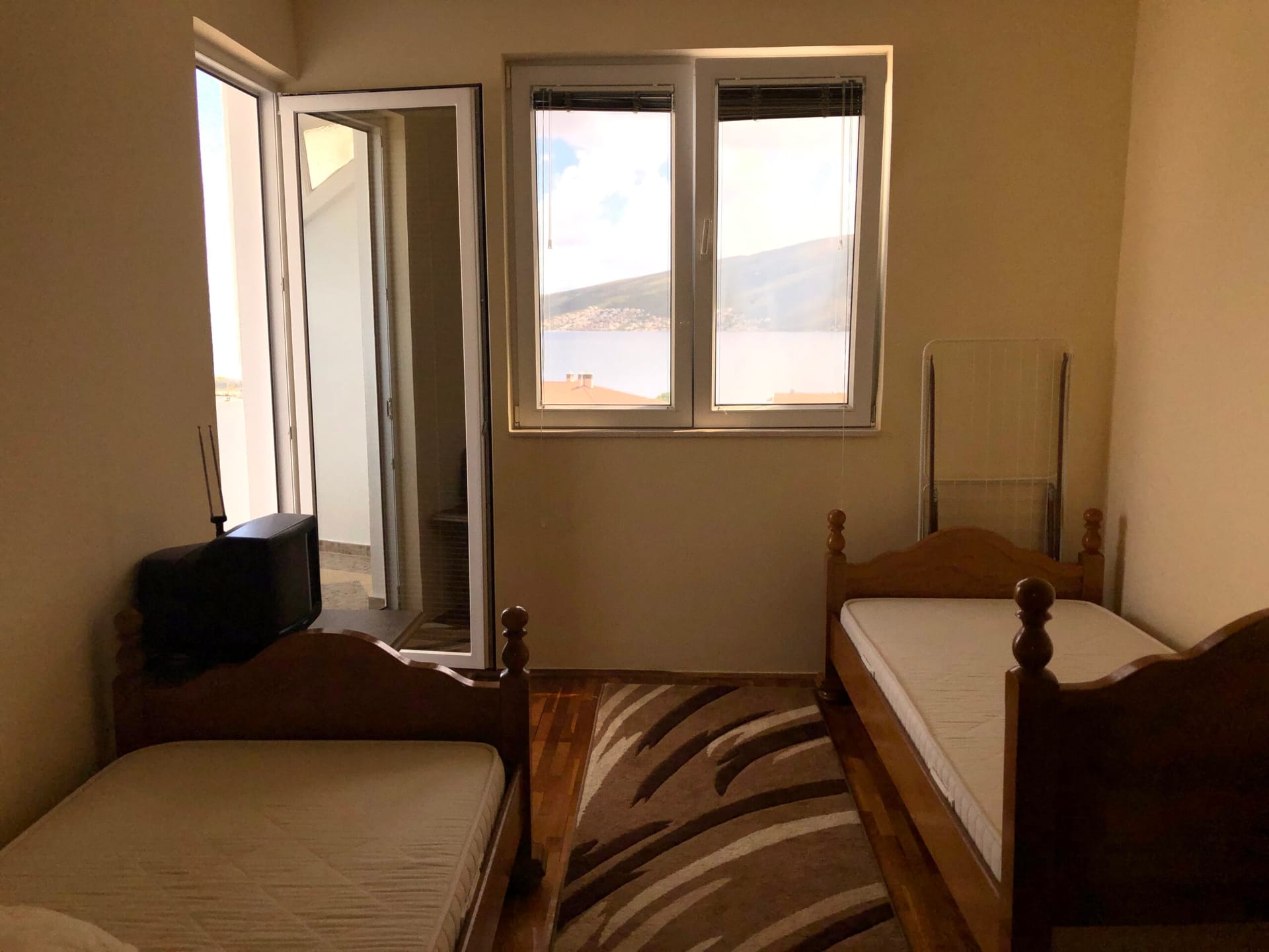 Bedroom in an apartment in Baošići, Montenegro: two wooden beds, parquet flooring, and sea view from the window and balcony.