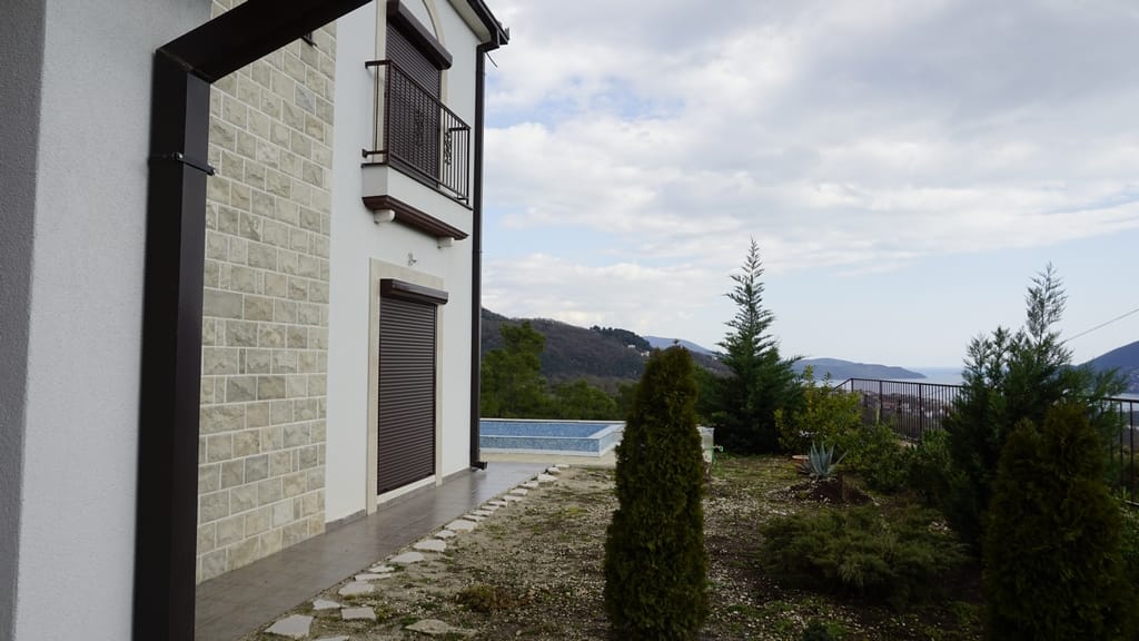 Façade de la villa à Igalo, Monténégro : parement en pierre, piscine, jardin et vue panoramique sur la mer et les montagnes.