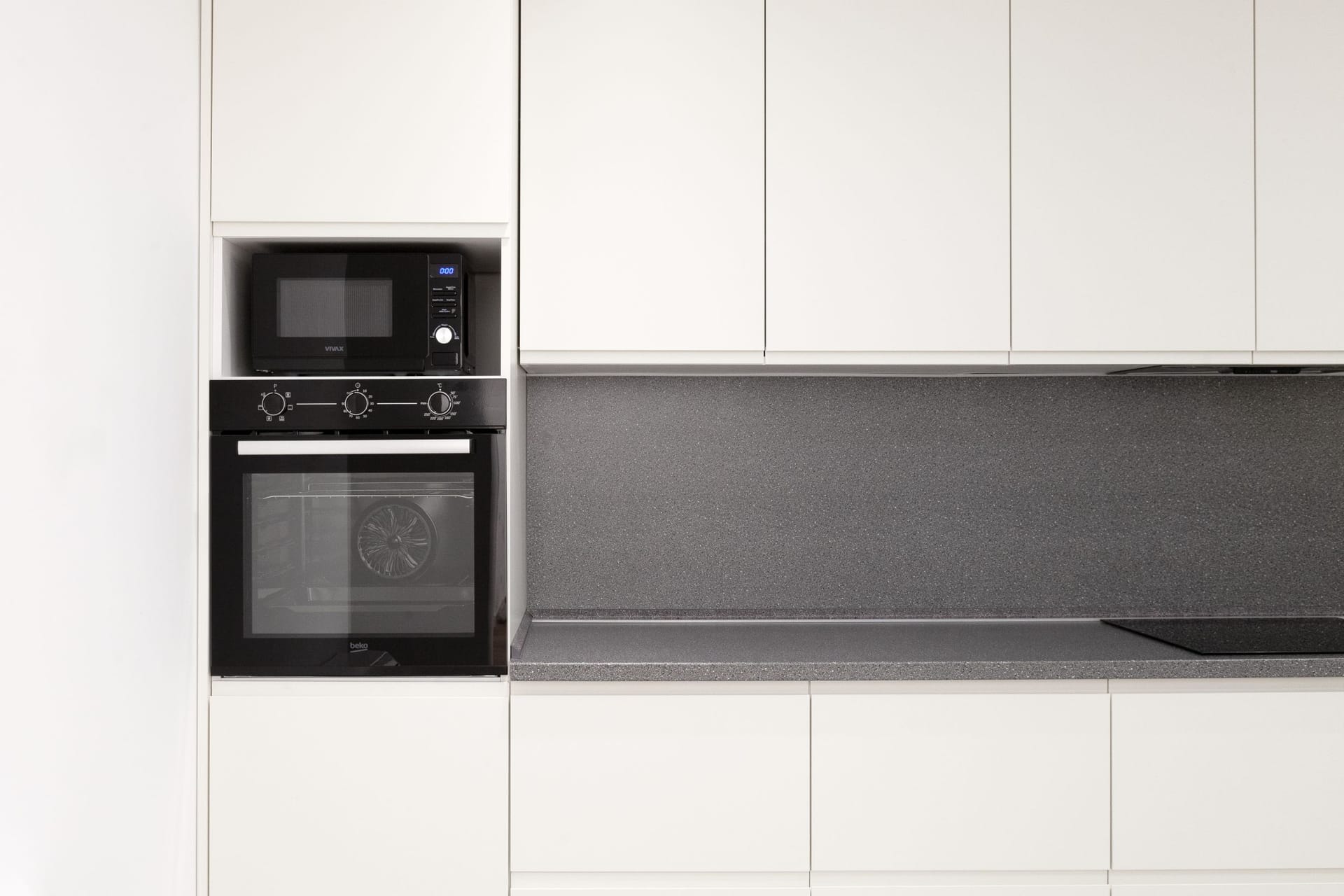 Современная белая кухня с серой столешницей и встроенной техникой Beko в квартире в Которе, Черногория.