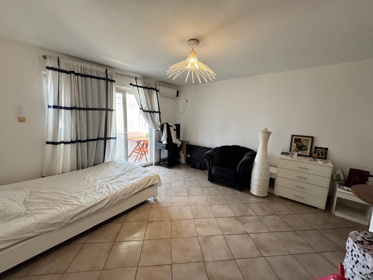 Bedroom in an apartment in Sveti Stefan, Montenegro: bed, armchair, dresser, tiled floor, and access to the balcony.