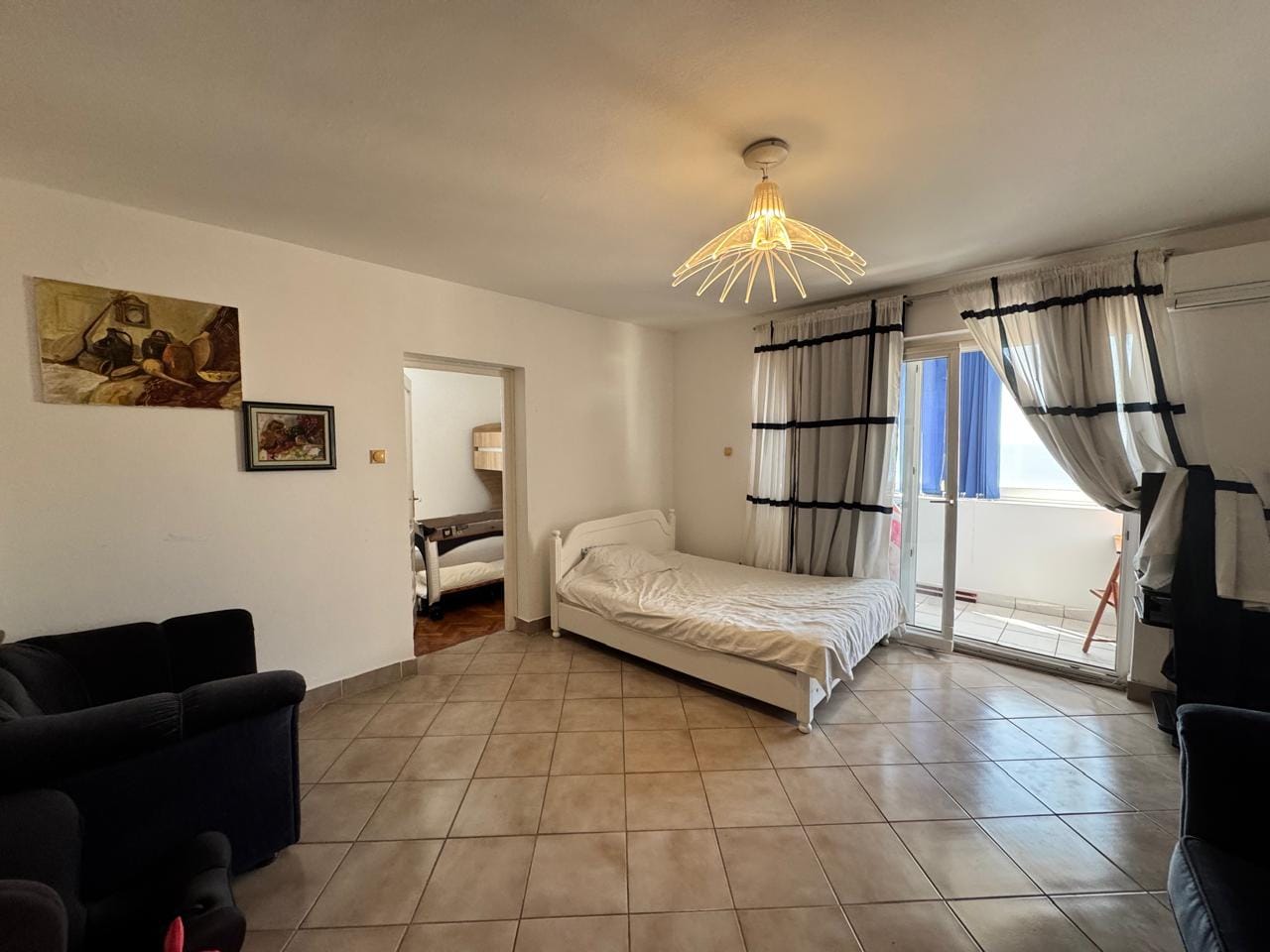 Bright living room with a bed and access to the balcony in an apartment, Sveti Stefan, Montenegro. Tiled floor, modern decor.