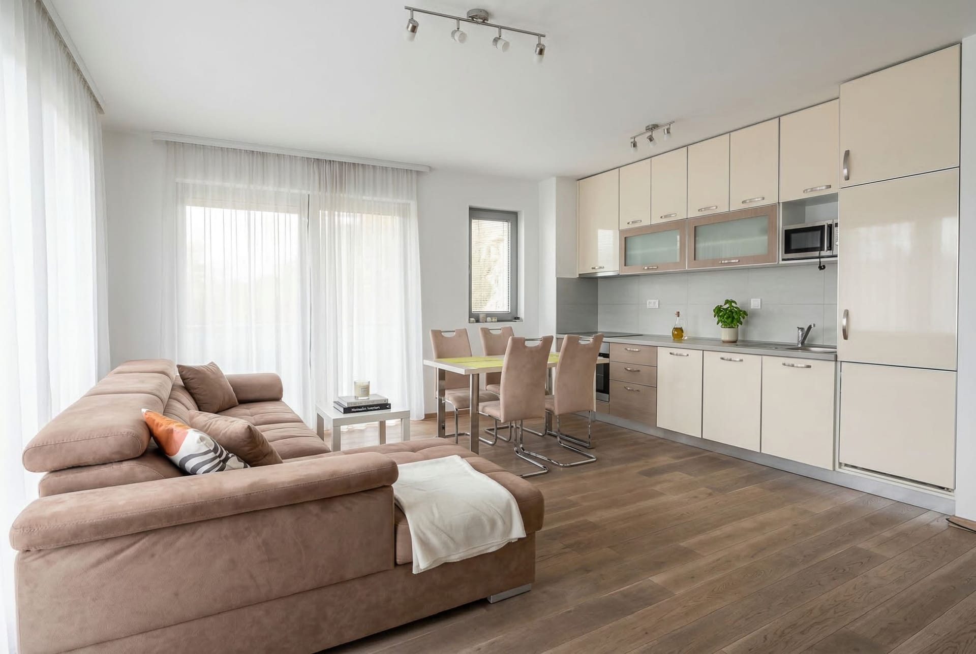 Modern living room with kitchen in an apartment in Pržno, Montenegro: brown sofa, dining area, and light-colored cabinetry.
