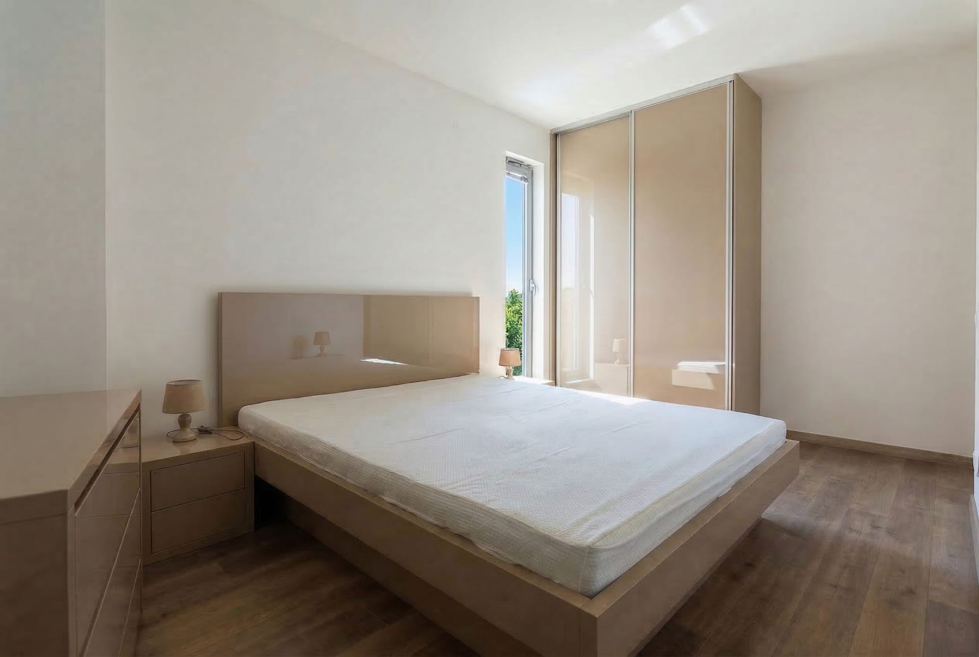 Bright bedroom in an apartment in Pržno, Montenegro: a double bed, glossy sliding wardrobe, and parquet flooring.