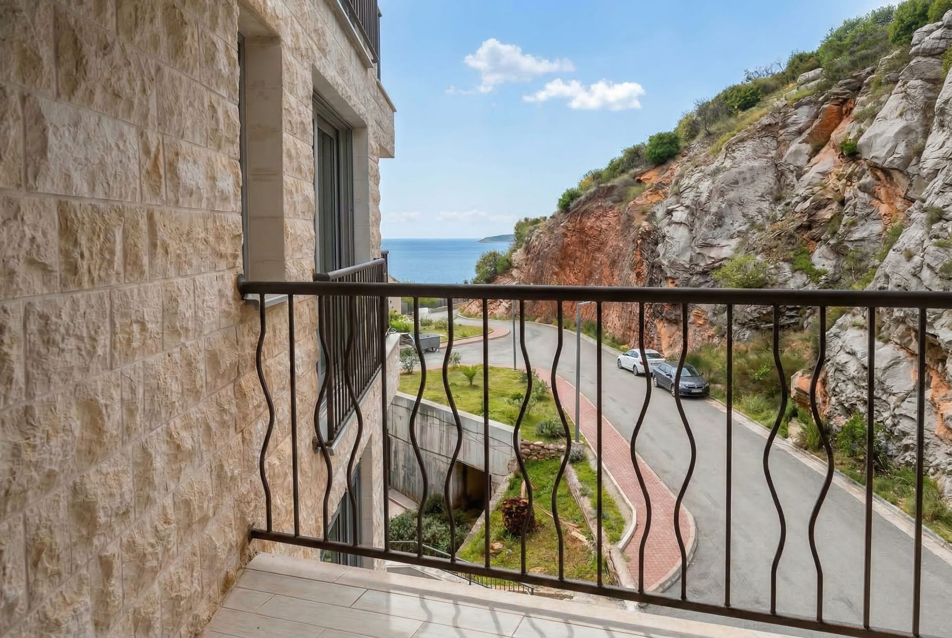 View from the apartment balcony in Pržno, Montenegro: stone facade finish, wrought-iron railings, road, and sea view.