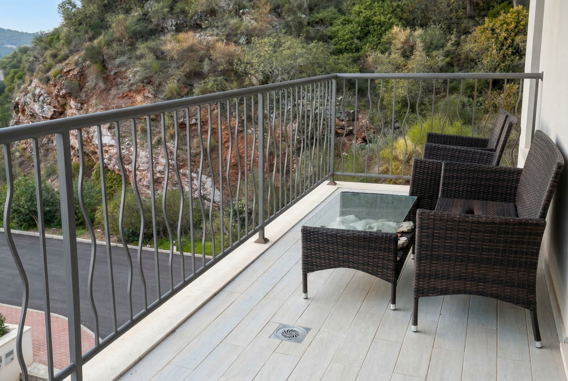 Balcony with wicker furniture and mountain views in an apartment in Pržno, Montenegro: light tile and wrought-iron railing.