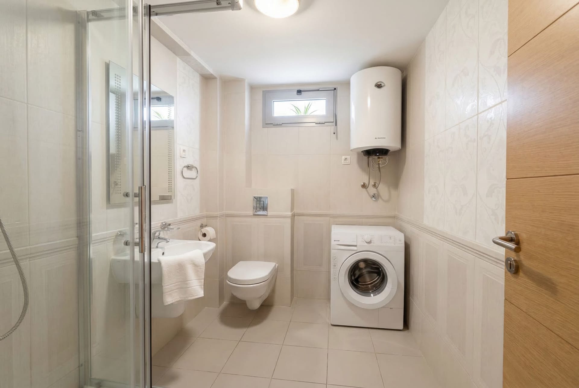 Bright bathroom in an apartment in Pržno, Montenegro: shower cabin, wall-mounted toilet, sink, and washing machine.