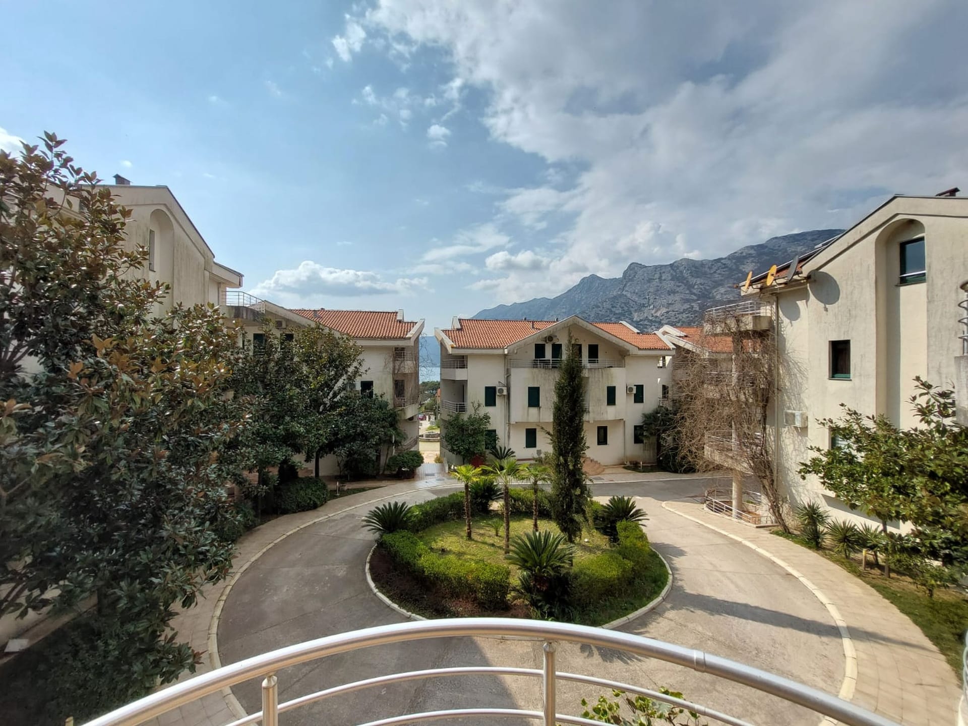 View from the balcony of the landscaped courtyard of a residential complex in Risan, Montenegro, with mountains and the sea on the horizon.