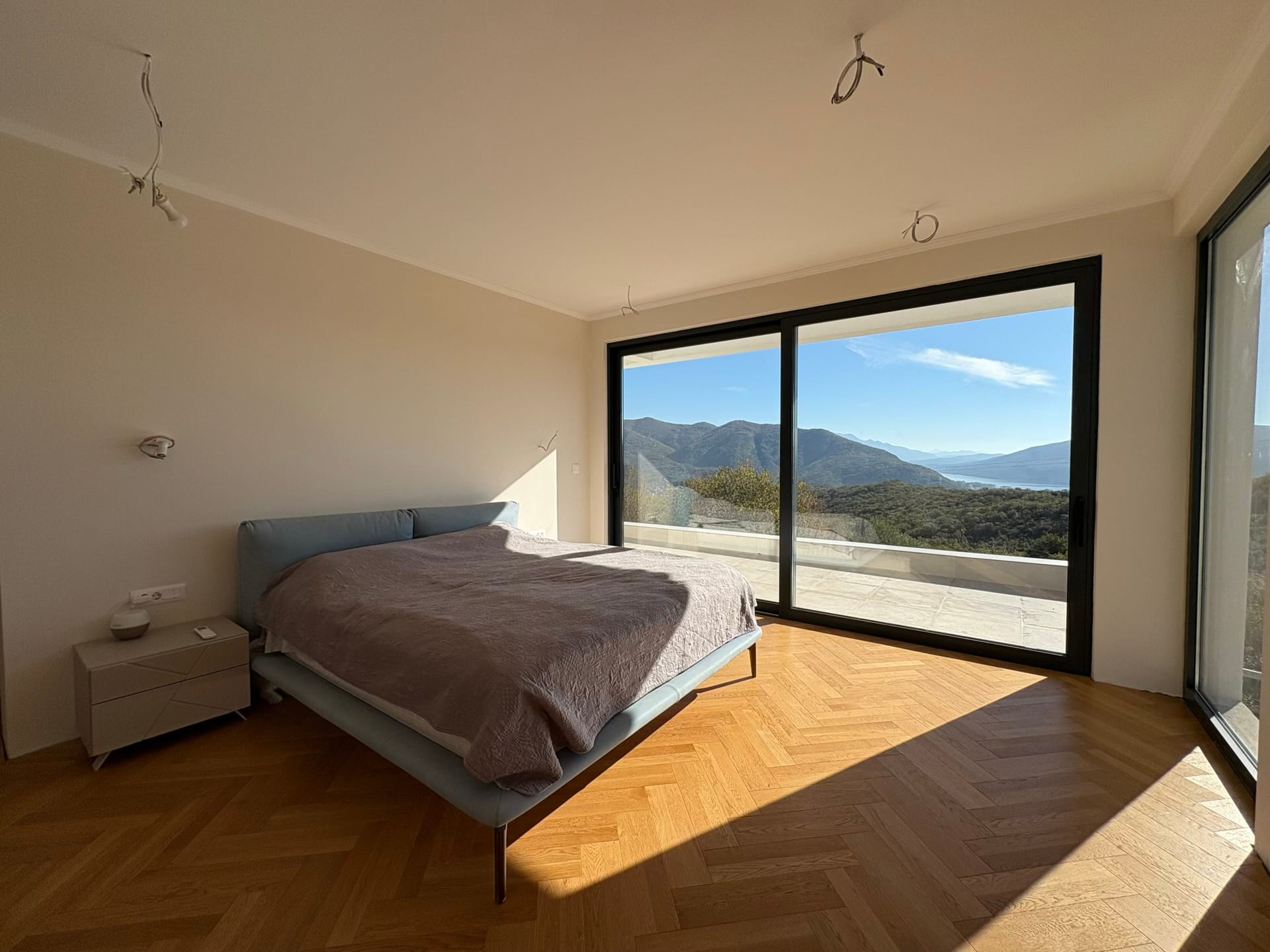 Bedroom in a villa in Herceg Novi, Montenegro: panoramic windows with mountain views, herringbone parquet, and a modern bed.