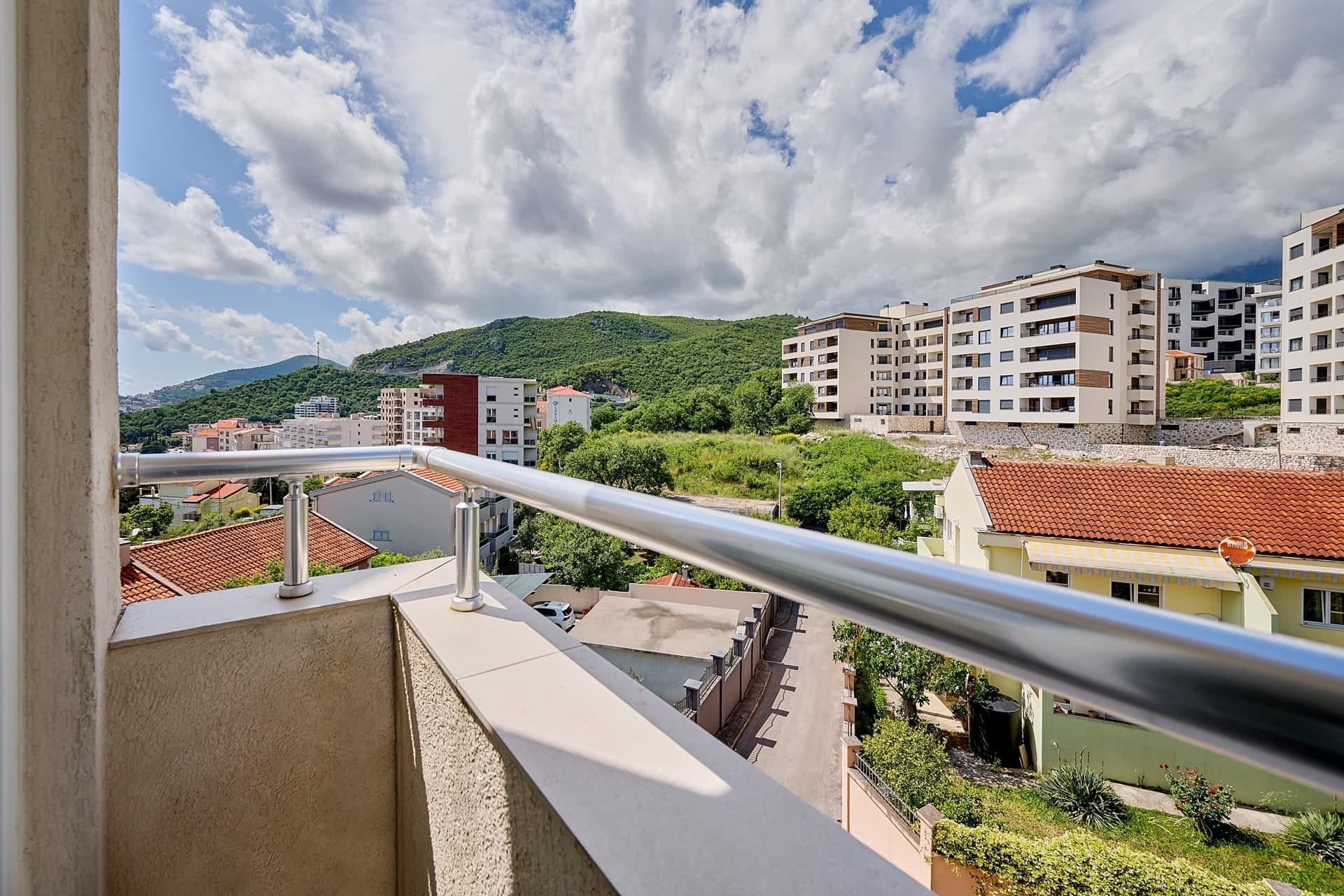 Pogled s balkona stana u Bečićima, Crna Gora: panorama planina, moderne gradnje i zelenih brežuljaka u sunčanom danu.