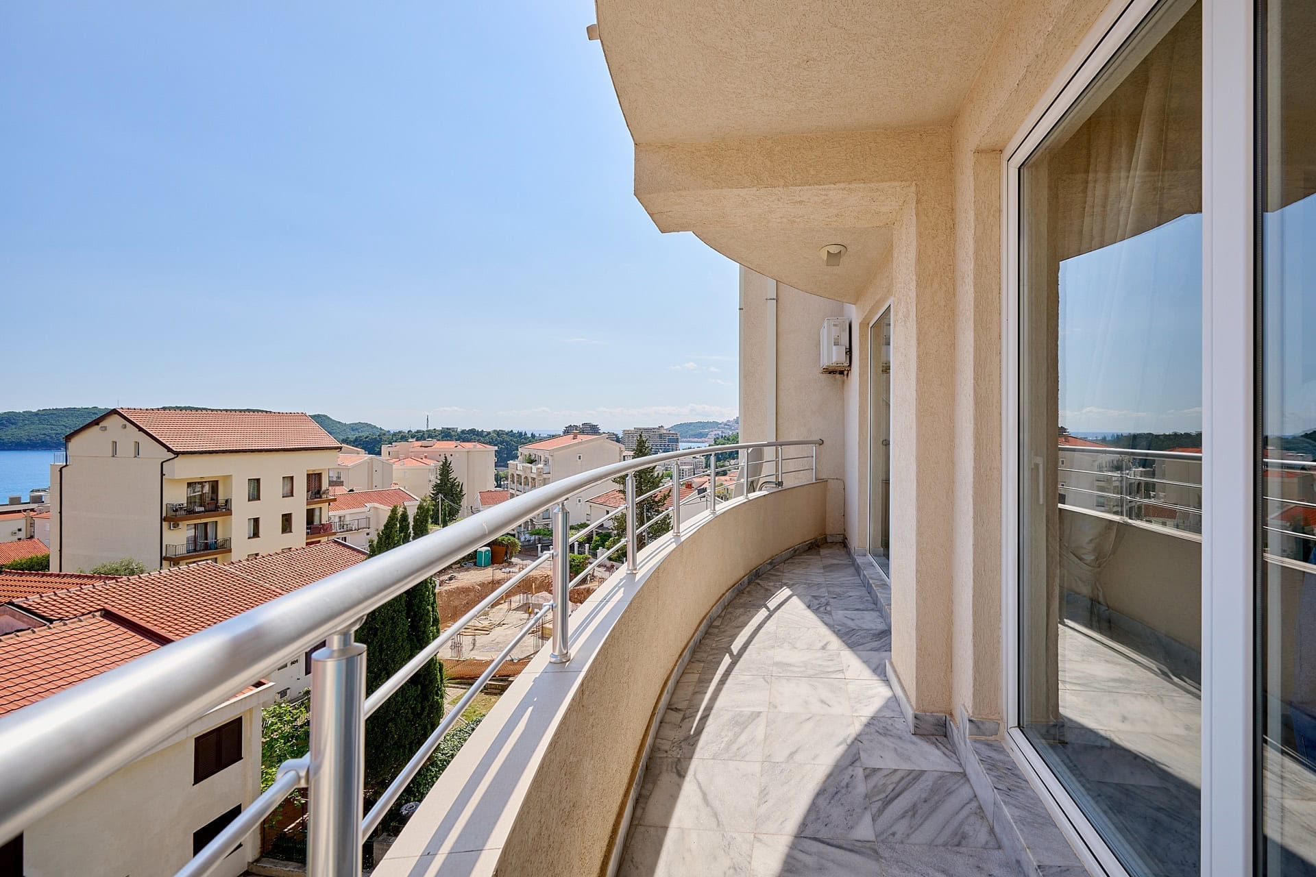 Prostran balkon sa mermernim podom i pogledom na more i grad Bečići, Crna Gora. Stan sa panoramskim staklenim zidovima.