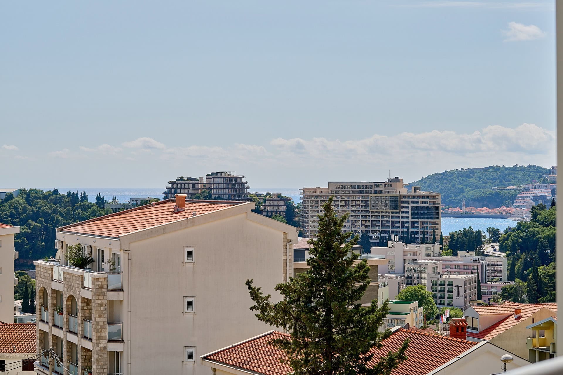 Panoramski pogled sa balkona stana u Bečićima, Crna Gora: gradska izgradnja, zeleni brežuljci i Jadransko more.