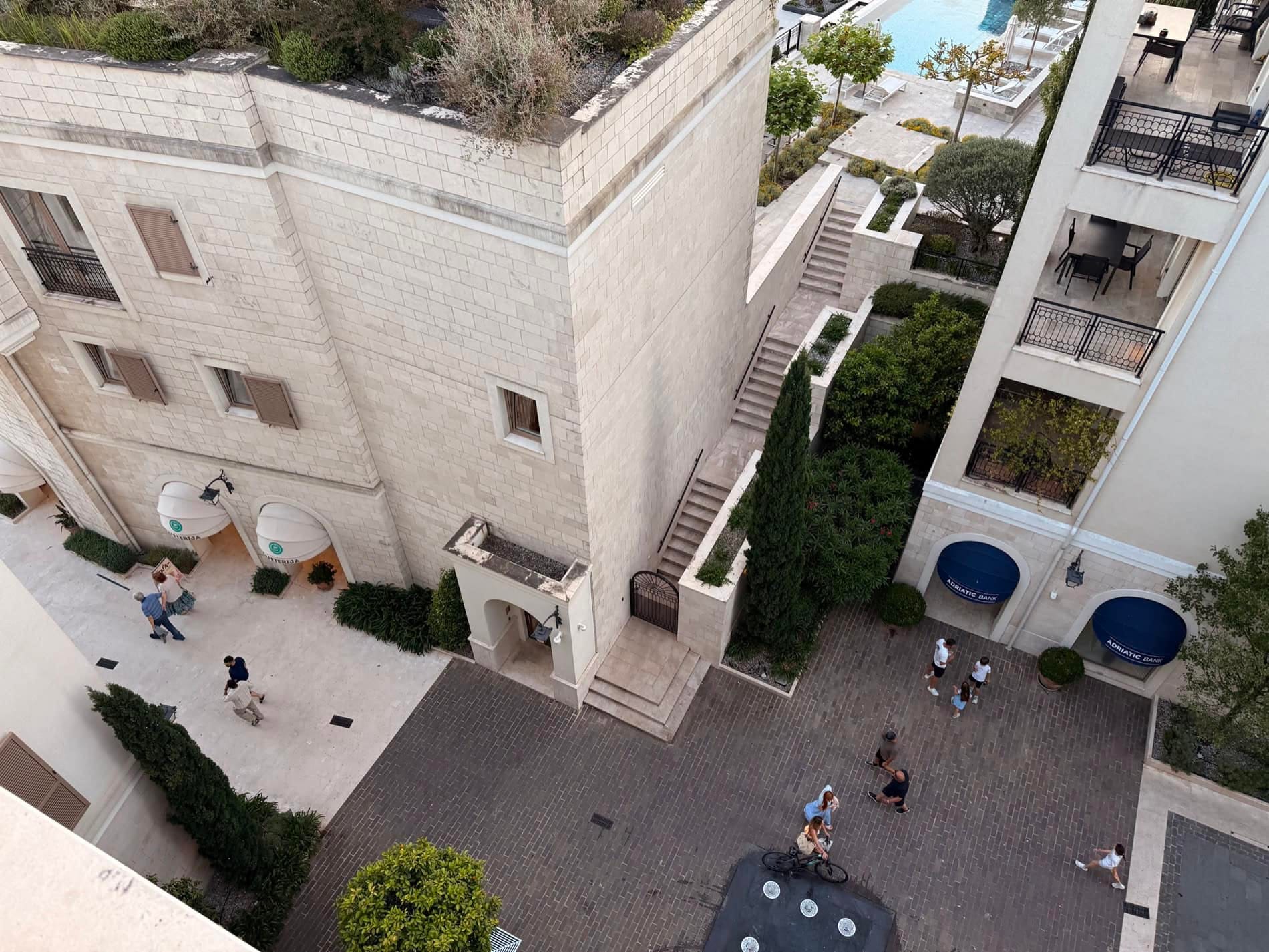 Вид сверху на жилой комплекс Porto Montenegro в Тивате, Черногория: каменные фасады, пешеходная площадь и бассейн.