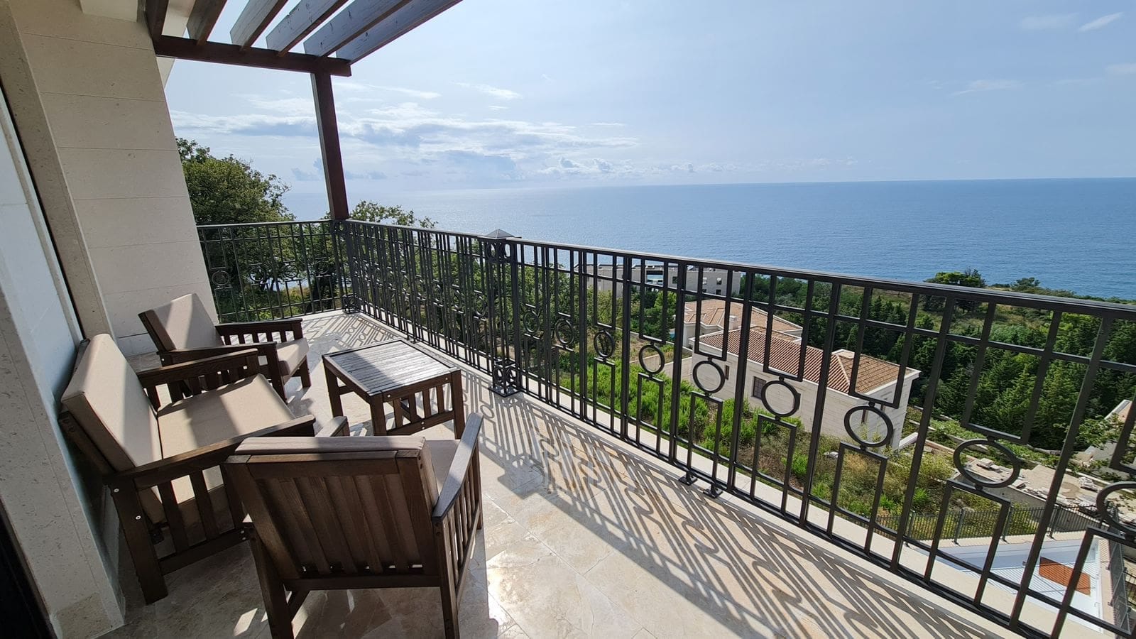 Villa balcony in Budva, Montenegro: wooden furniture, stone floor, and panoramic view of the Adriatic Sea.