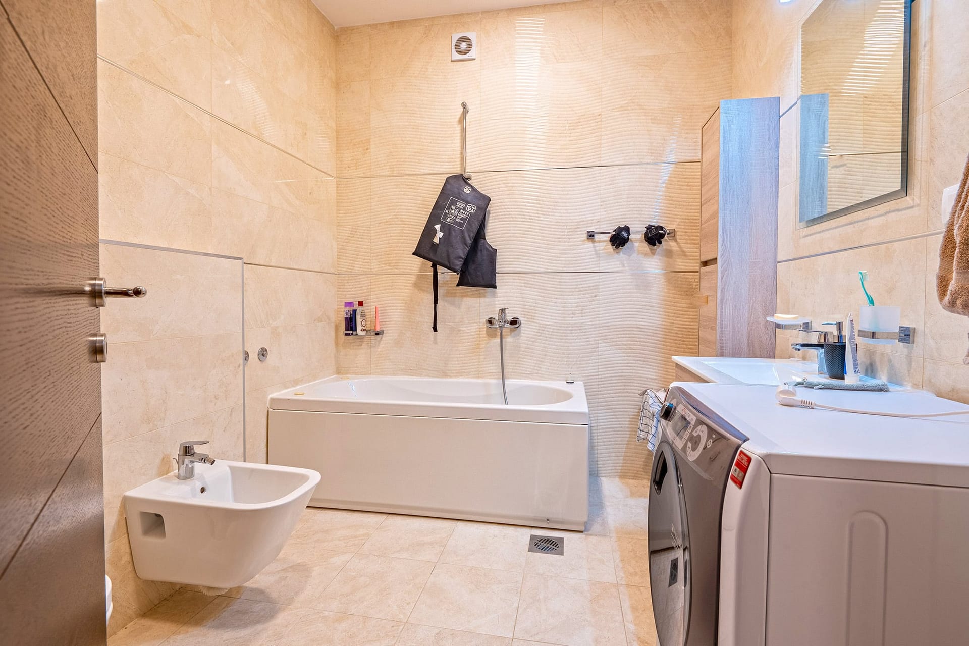 Modernes Badezimmer mit weißer Badewanne, Bidet und Waschmaschine in einer Wohnung in Budva, Montenegro. Beige Fliesen.