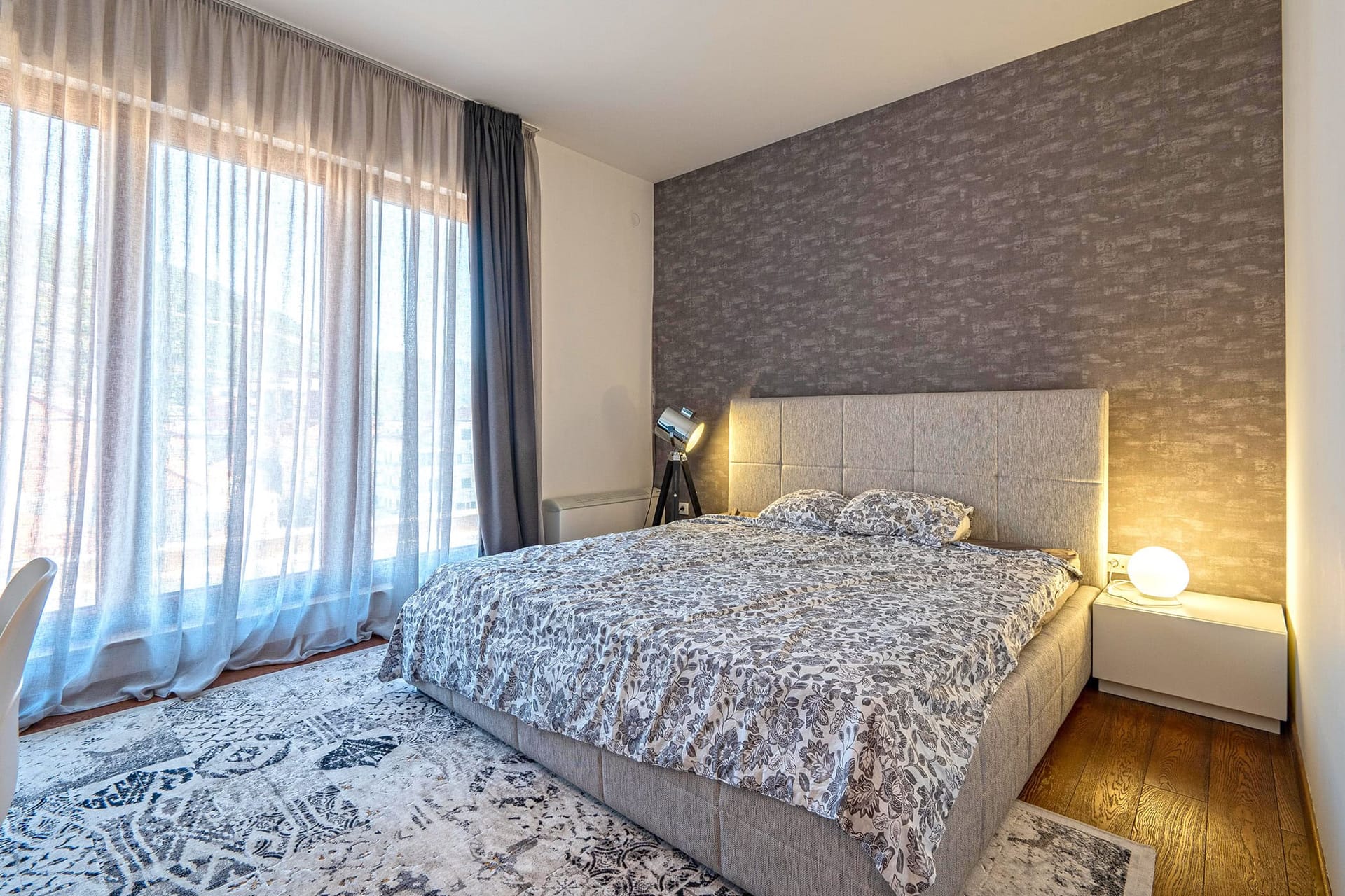Modernes Schlafzimmer mit Doppelbett in einer Wohnung in Budva, Montenegro: Panoramafenster, stilvolle Dekoration und Beleuchtung.