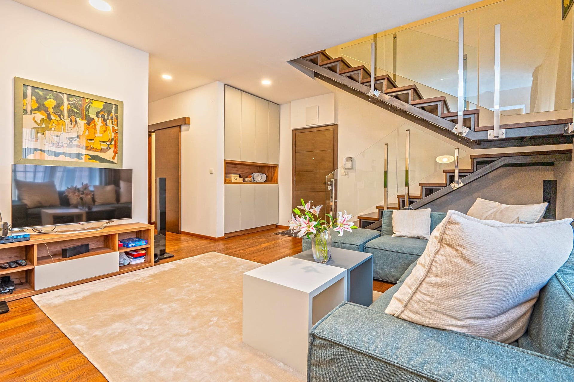 Wohnzimmer in einem Duplex in Budva, Montenegro: moderne Möbel, helles Sofa und stilvolle Treppe mit Glas.