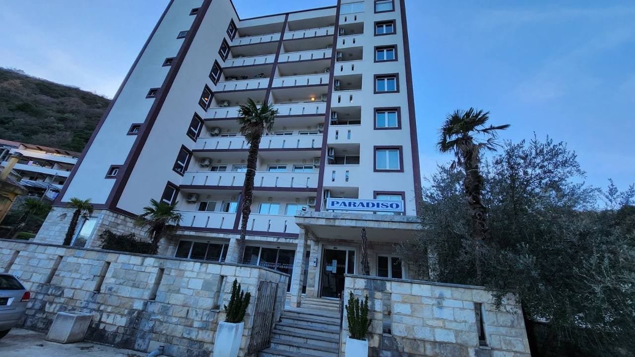 Фасад многоэтажного жилого комплекса Paradiso в Бечичи, Черногория, с балконами и пальмами у входа.