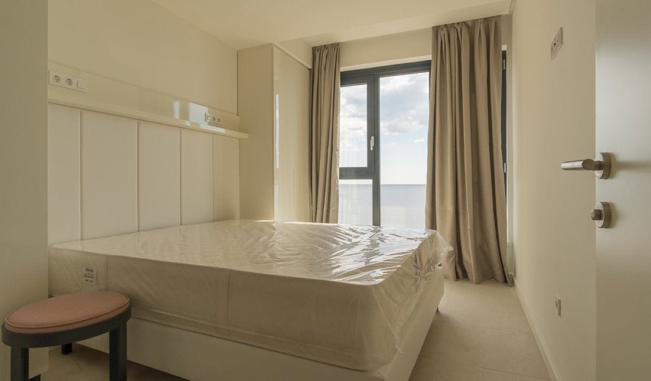 Spavaća soba u apartmanima Bečići, Crna Gora: svetla završna obrada, bračni krevet i panoramski prozor s pogledom na more.