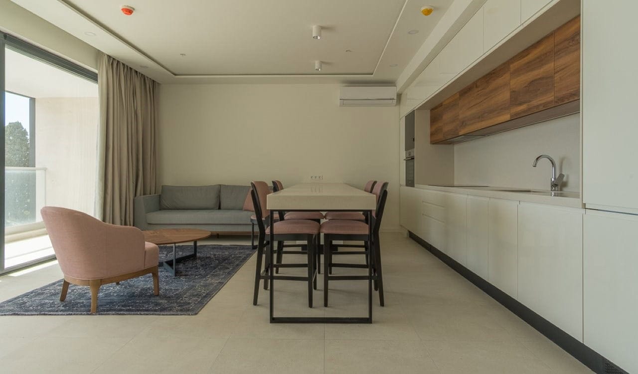 Savremeni dnevni boravak sa kuhinjom u apartmanu u Bečićima, Crna Gora: svetao enterijer, mekani nameštaj i terasa.