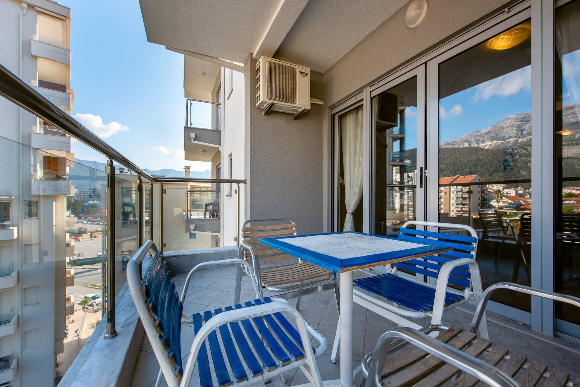 Balkon z meblami w mieszkaniu w Budvie, Czarnogóra, z panoramicznym widokiem na góry i miasto.