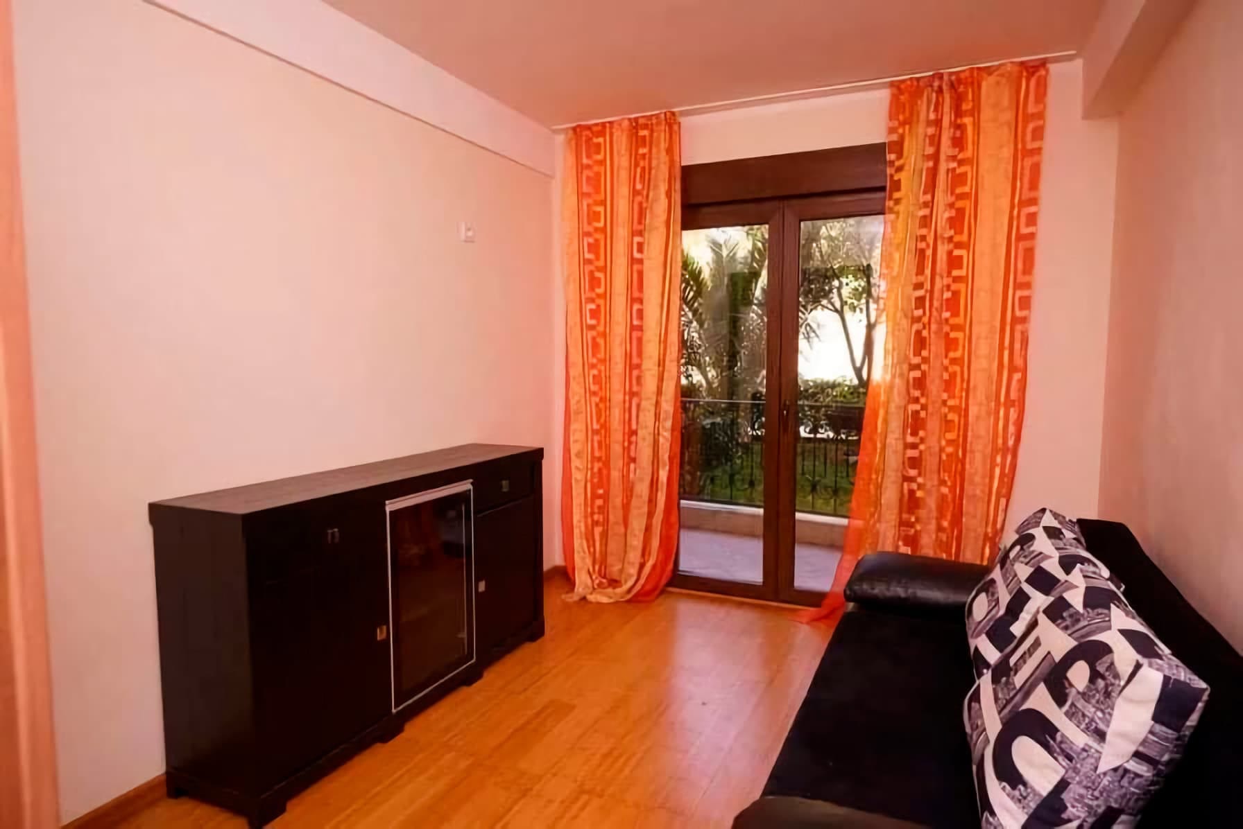 Dnevna soba u stanu u Budvi, Crna Gora: tamni nameštaj, sofa s printom, izlaz na balkon s pogledom na zelenilo.