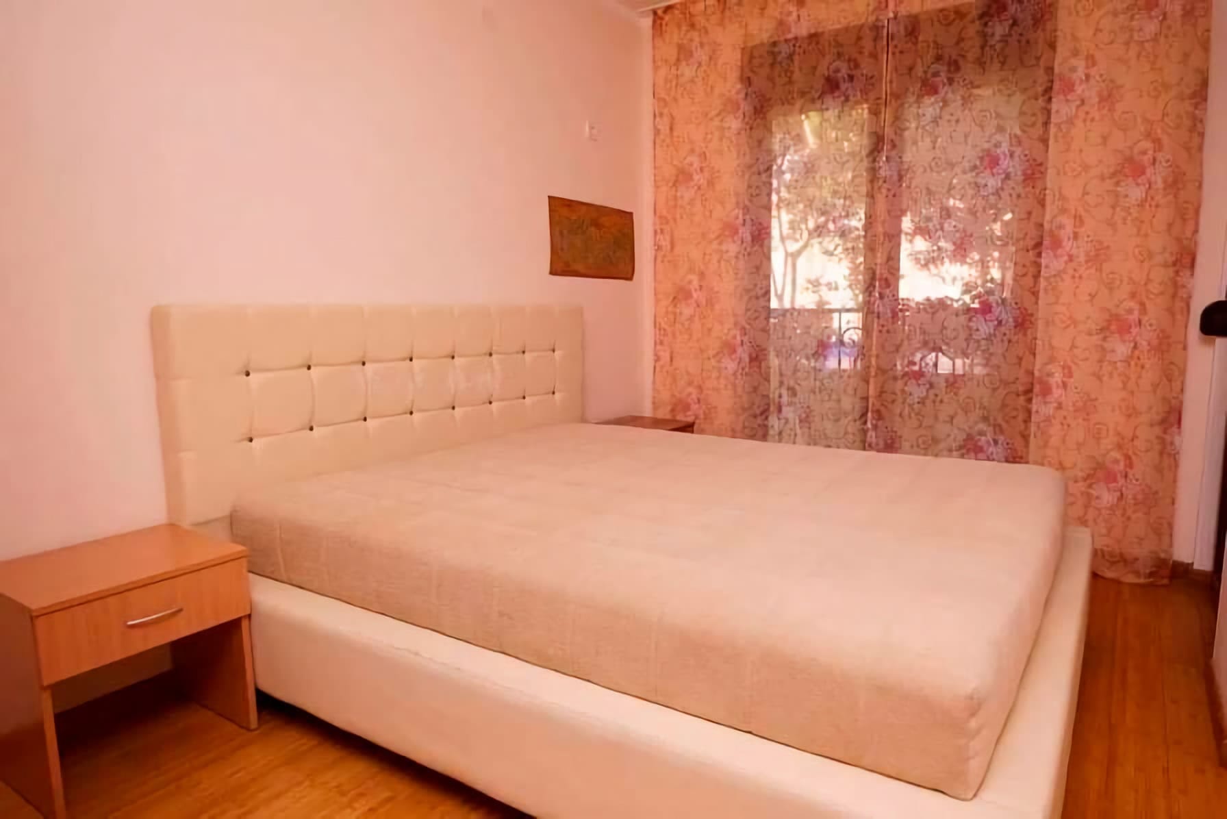 Spavaća soba sa bračnim krevetom i noćnim stočićem u stanu u Budvi, Crna Gora, sa izlazom na balkon.
