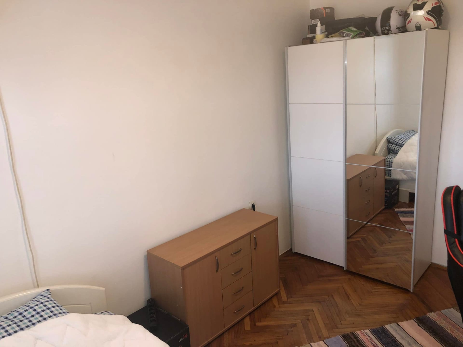 Chambre dans un appartement à Herceg Novi, Monténégro : armoire blanche avec miroir, commode en bois et parquet en chevrons.